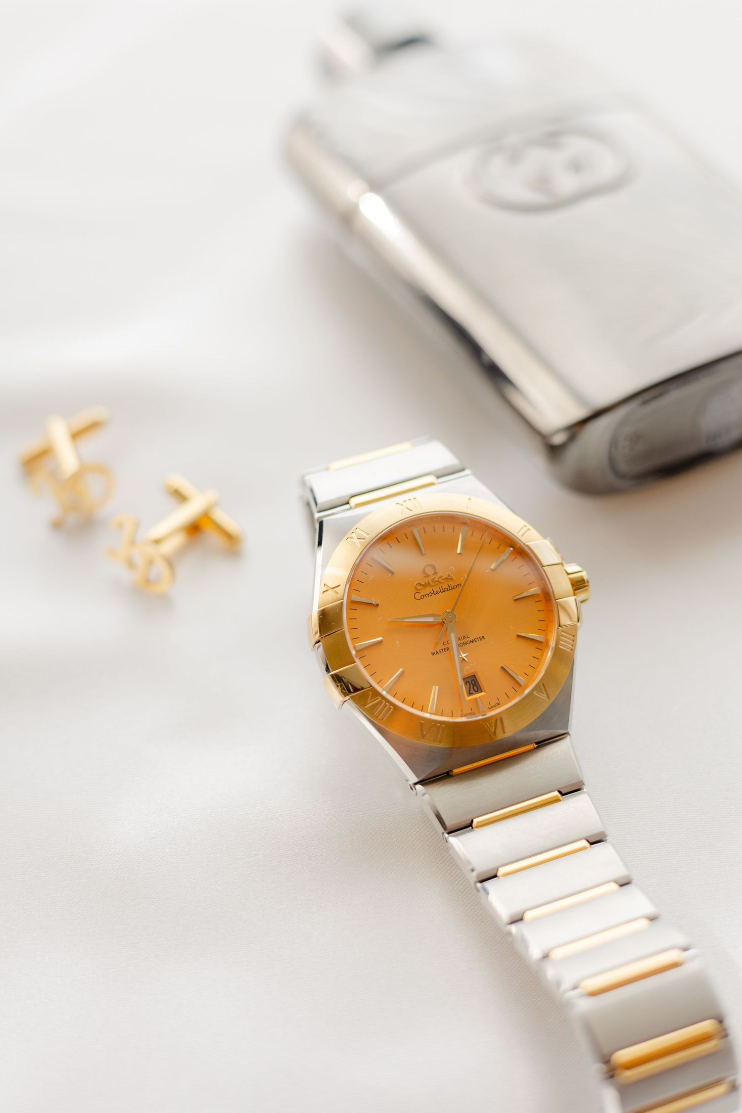 Gold and silver luxury watch with orange face displayed with cufflinks on white surface.
