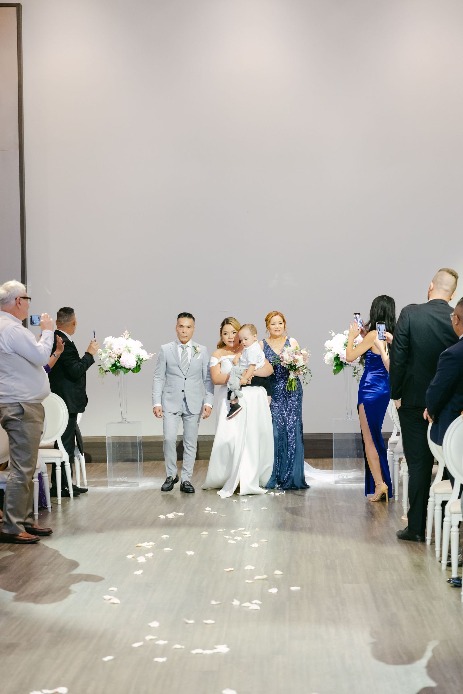 Wedding ceremony processional in a modern venue with white chairs and floral decorations.