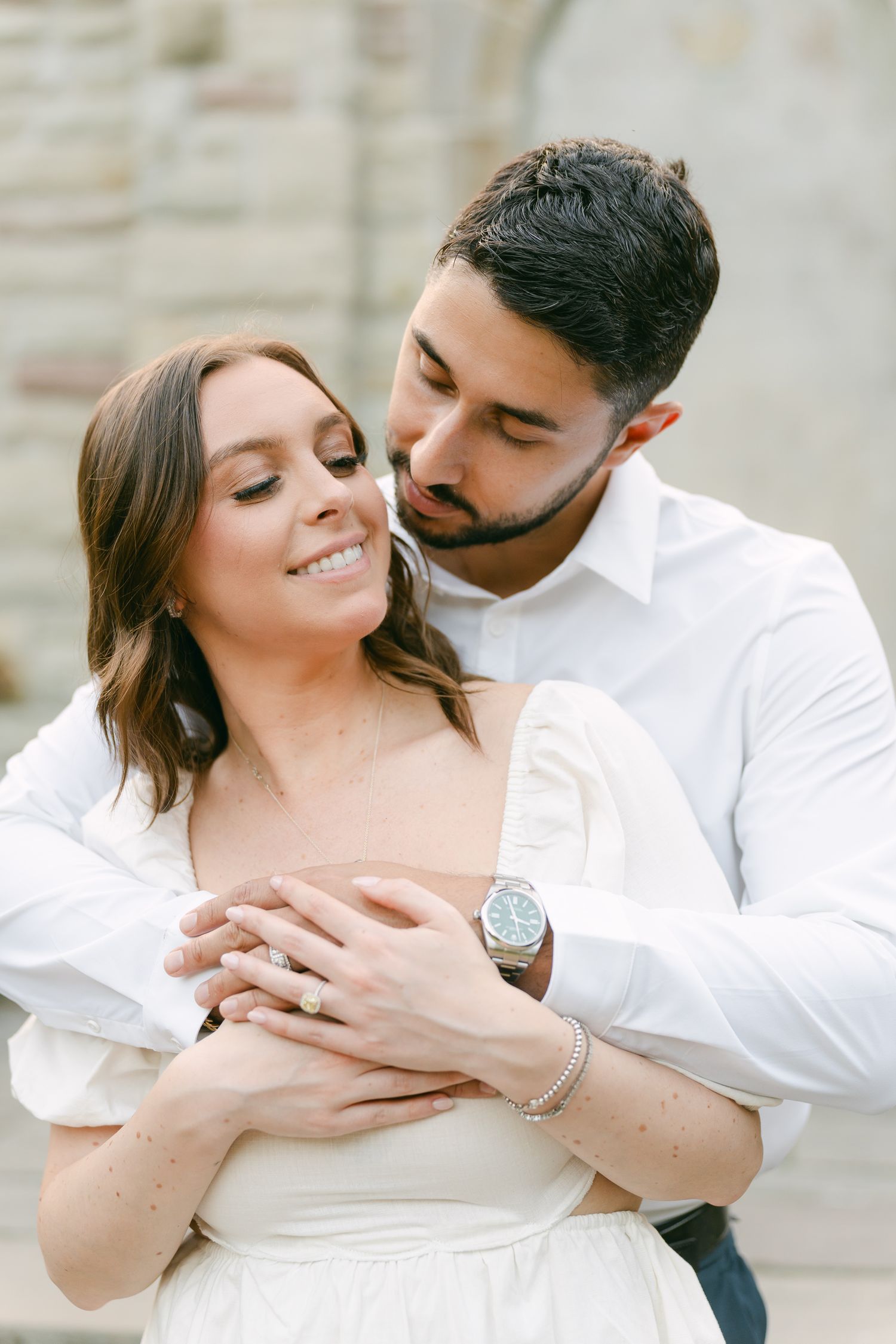 Intimate engagement photo of a couple embracing against a stone wall backdrop.