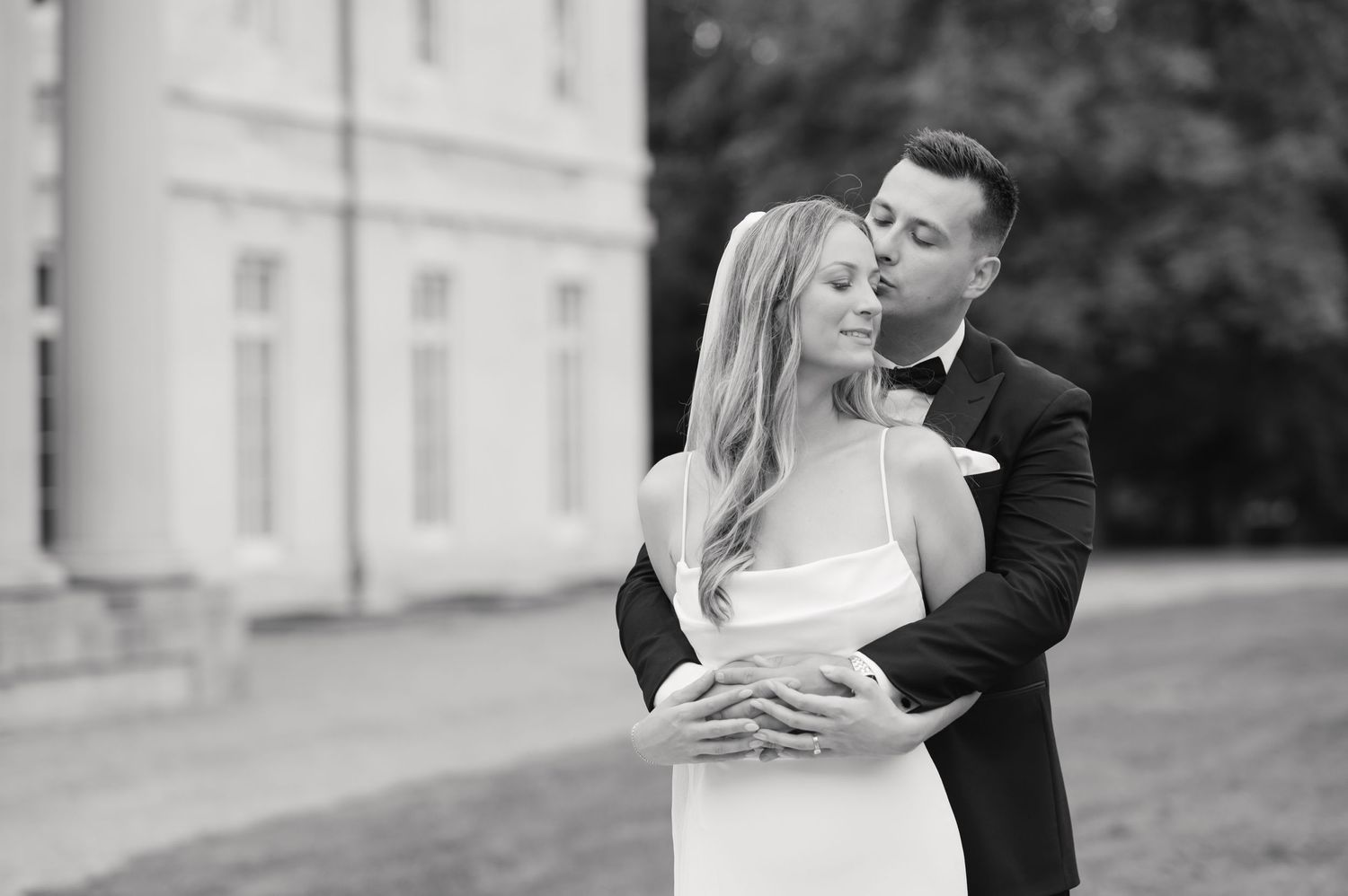 Black and white portrait of couple sharing intimate moment outside historic building.