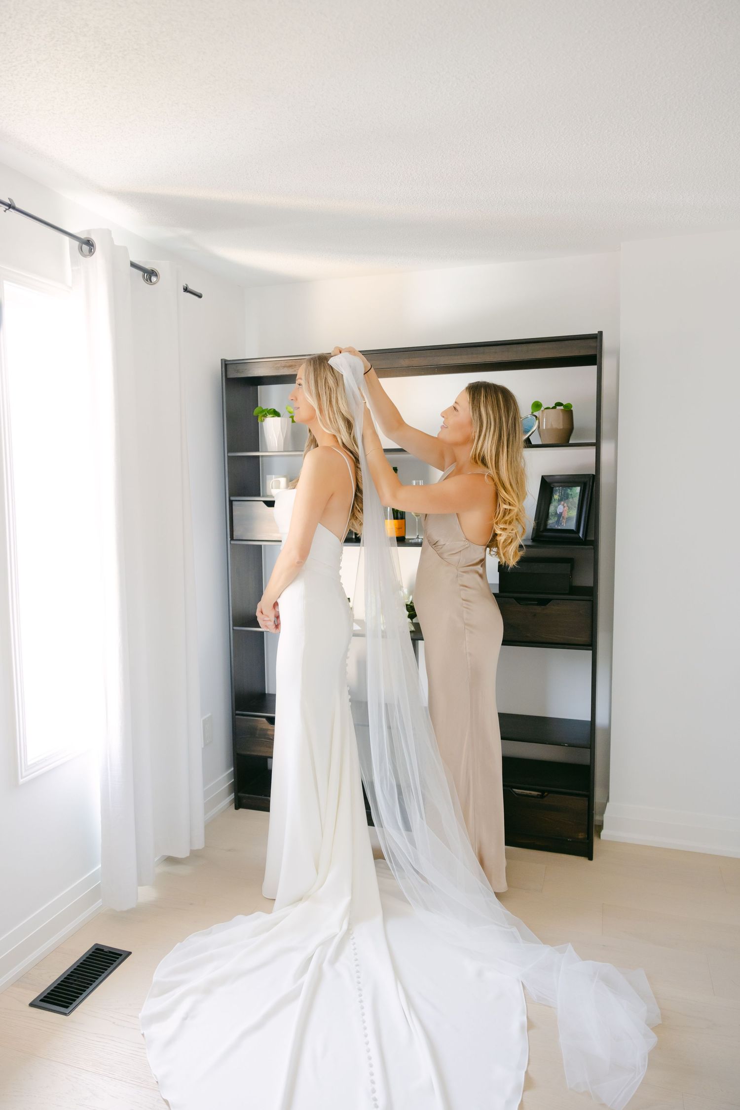 Final wedding veil adjustments being made in bright modern room with floating shelves.