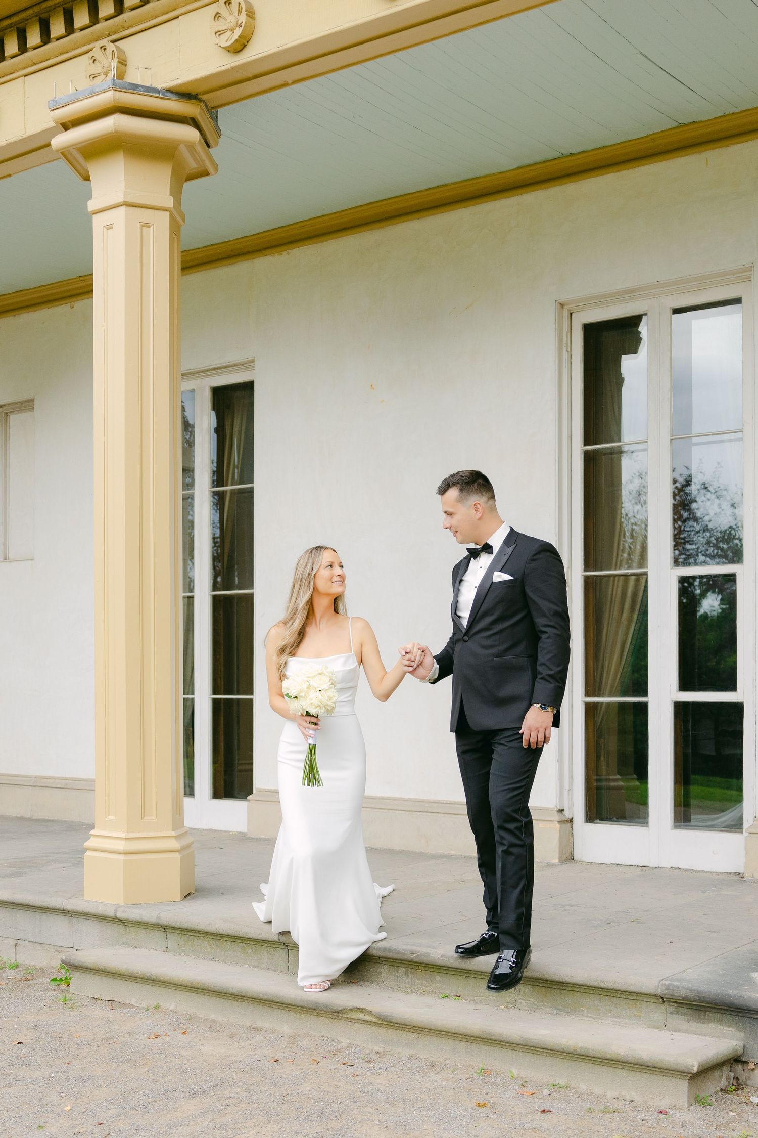 Couple descending stone steps in elegant wedding attire at historic venue.