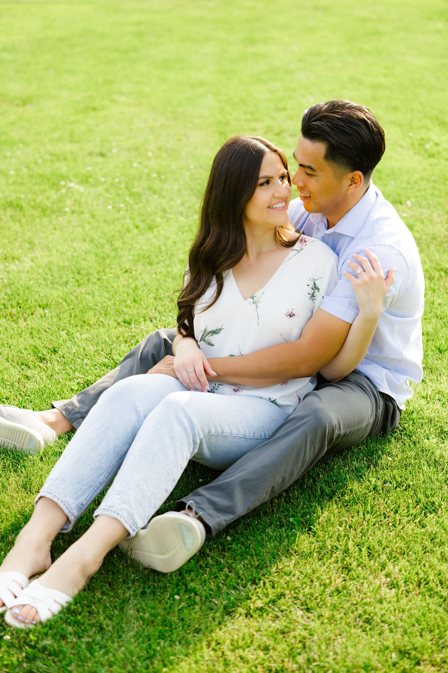 A couple relaxes together on green grass during a sunny outdoor photoshoot.
