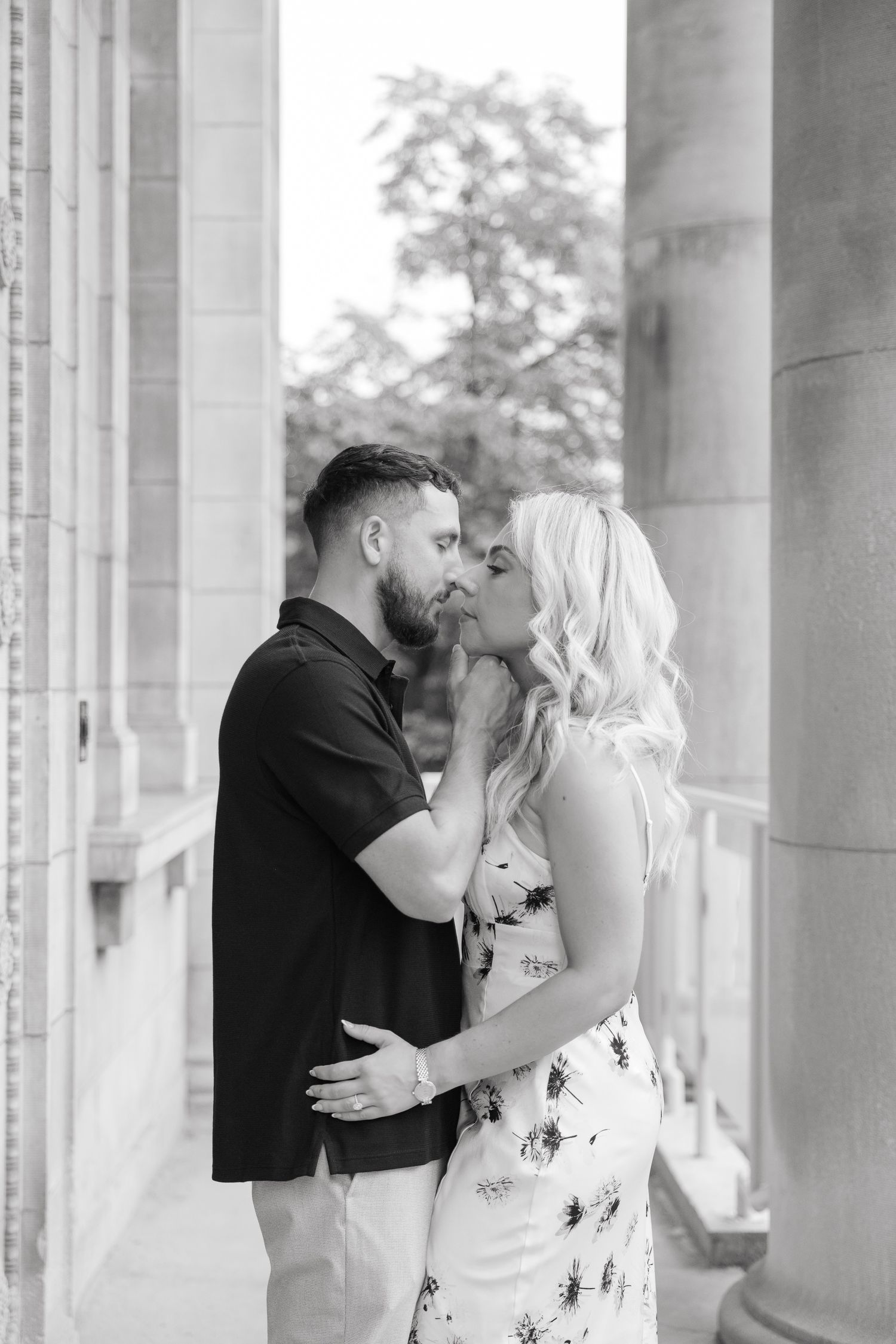 Romantic black and white portrait of a couple sharing a tender moment between stone pillars.