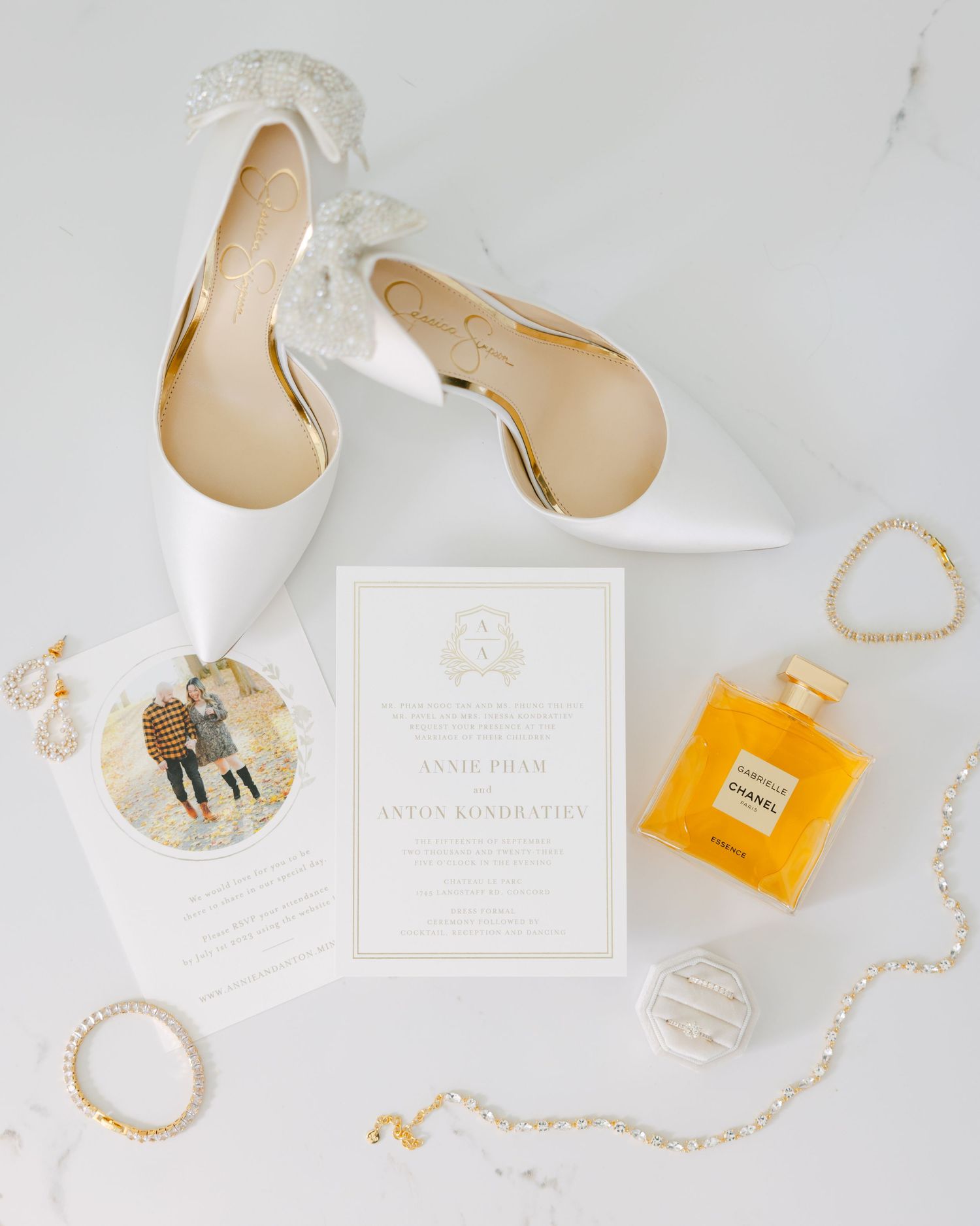 Wedding details flatlay with white heels, invitation, perfume bottle and gold jewelry on marble.