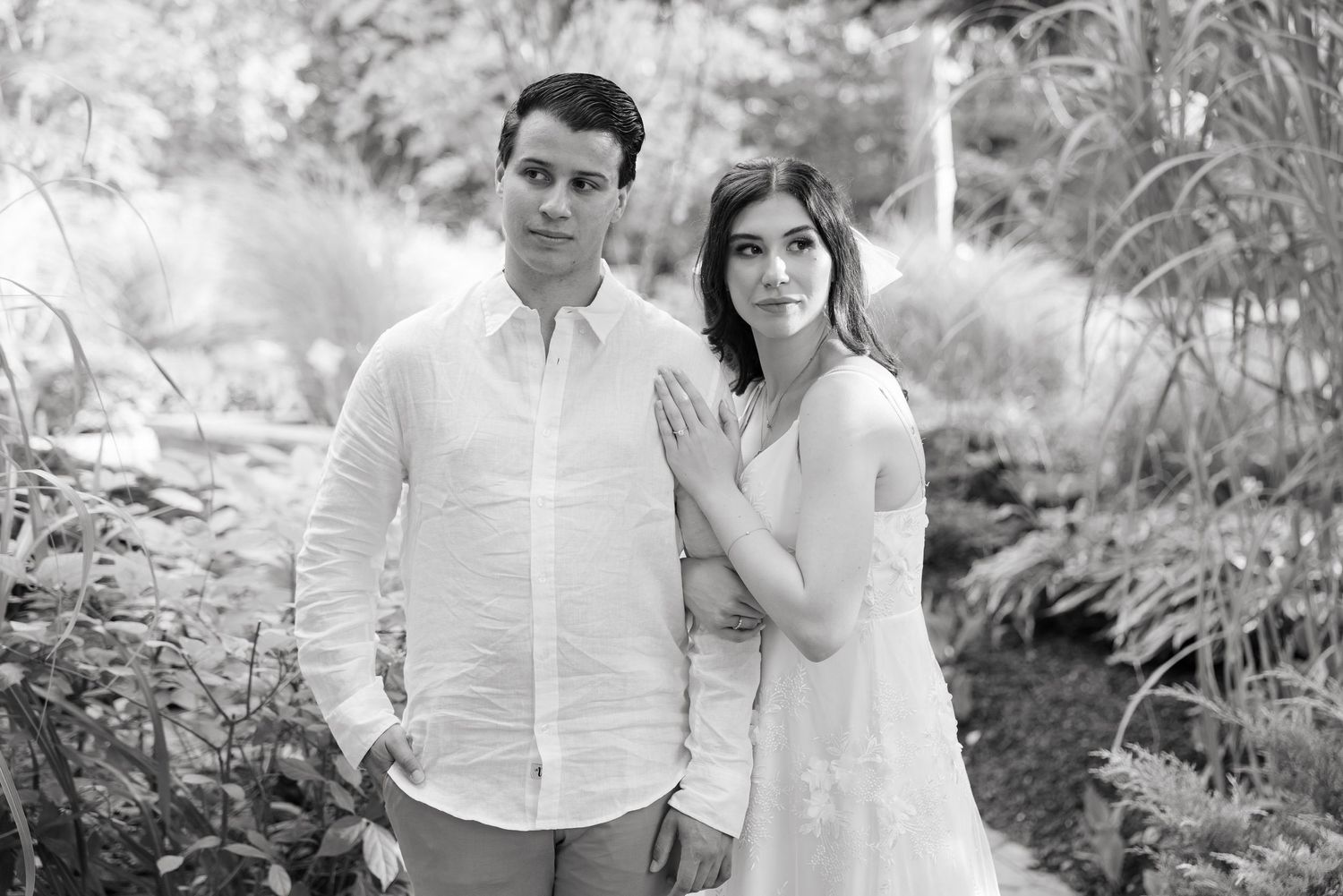 A romantic black and white portrait of a couple in a lush garden setting.
