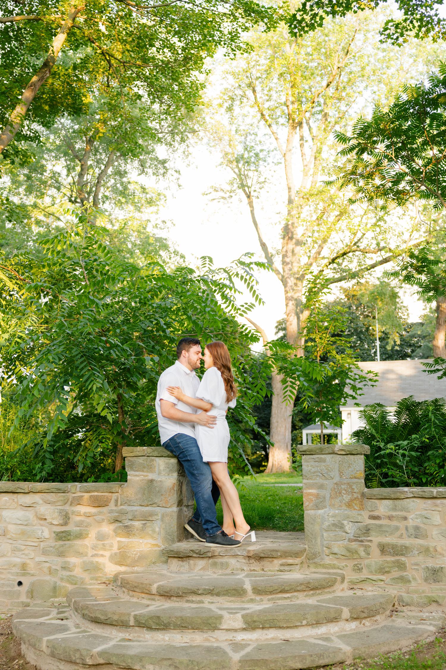 Two people share an intimate moment on decorative stone steps in a peaceful garden setting.