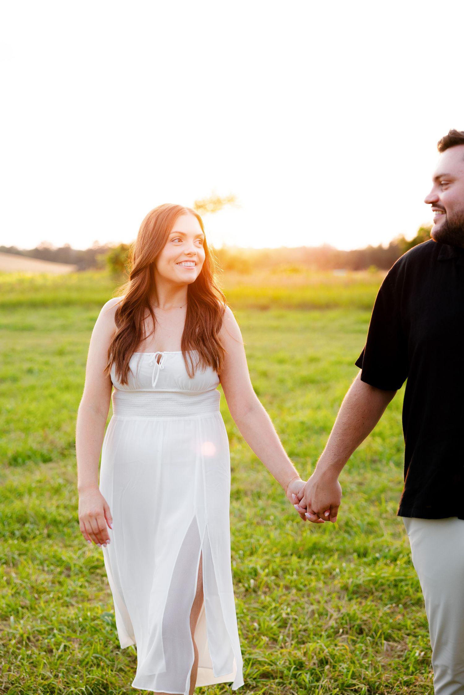 A couple shares a joyful moment walking through a sun-drenched field at golden hour.