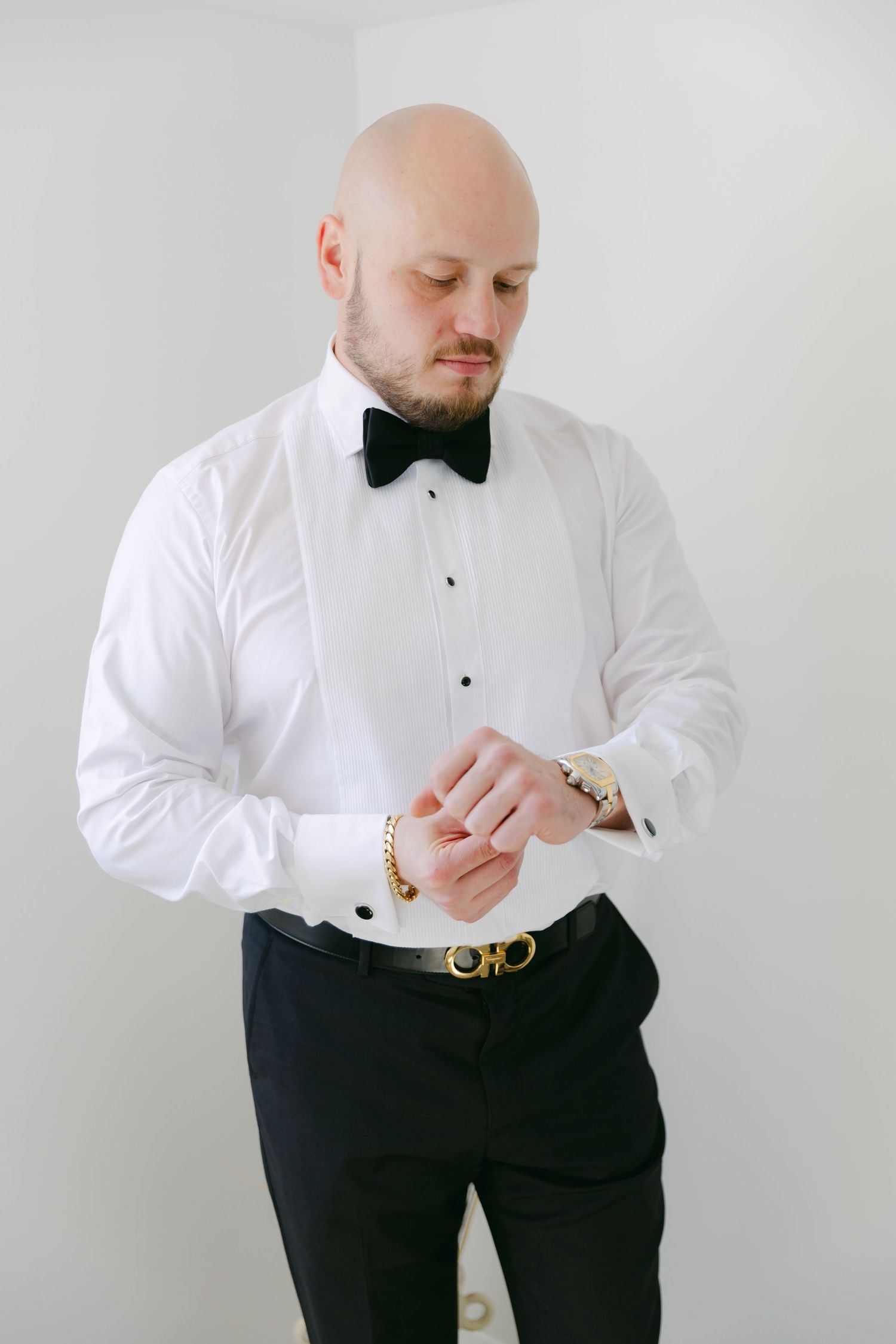 Person in formal attire checking watch while wearing bow tie and suspenders.