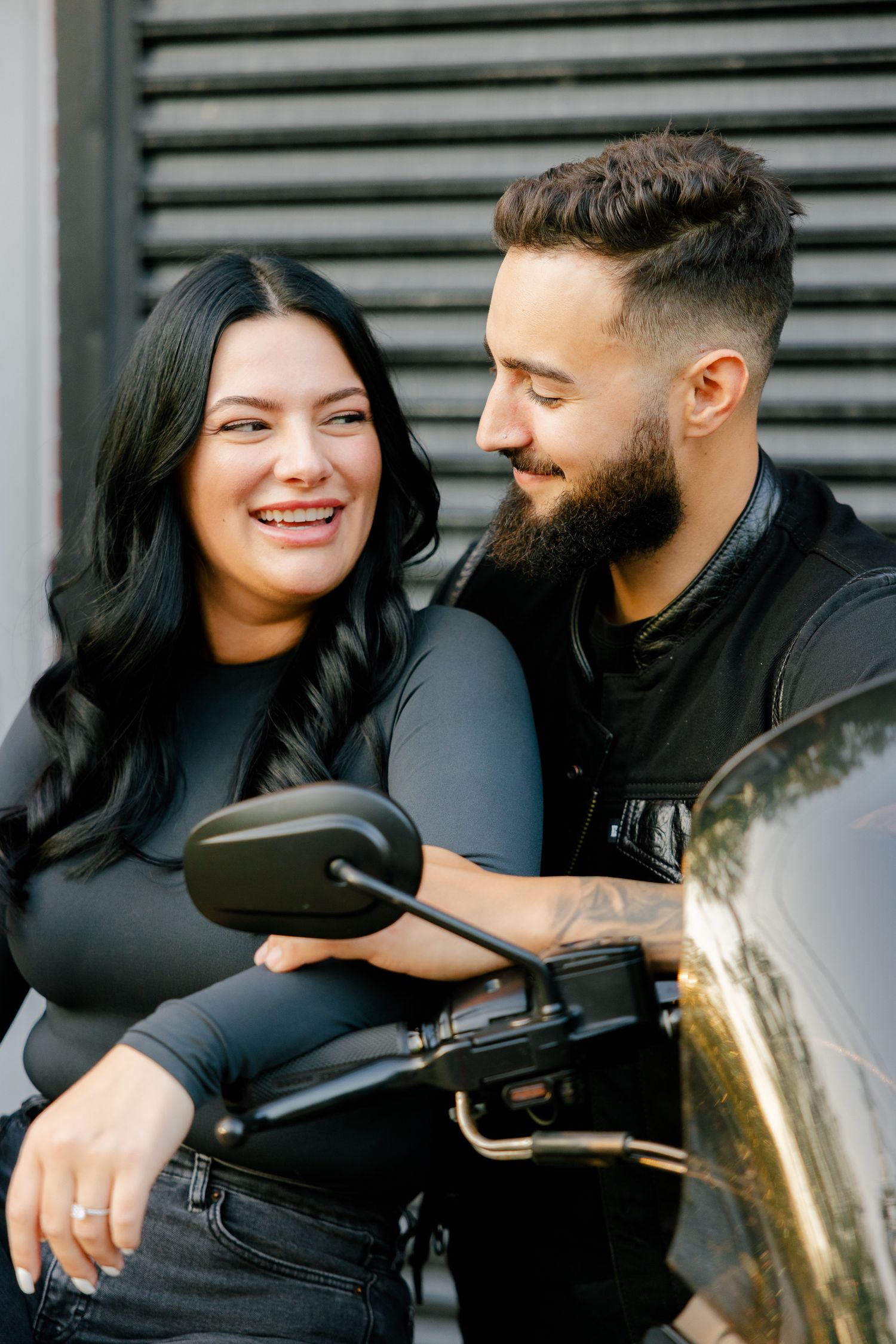 Candid moment captured of two people sharing a laugh by their motorcycle.