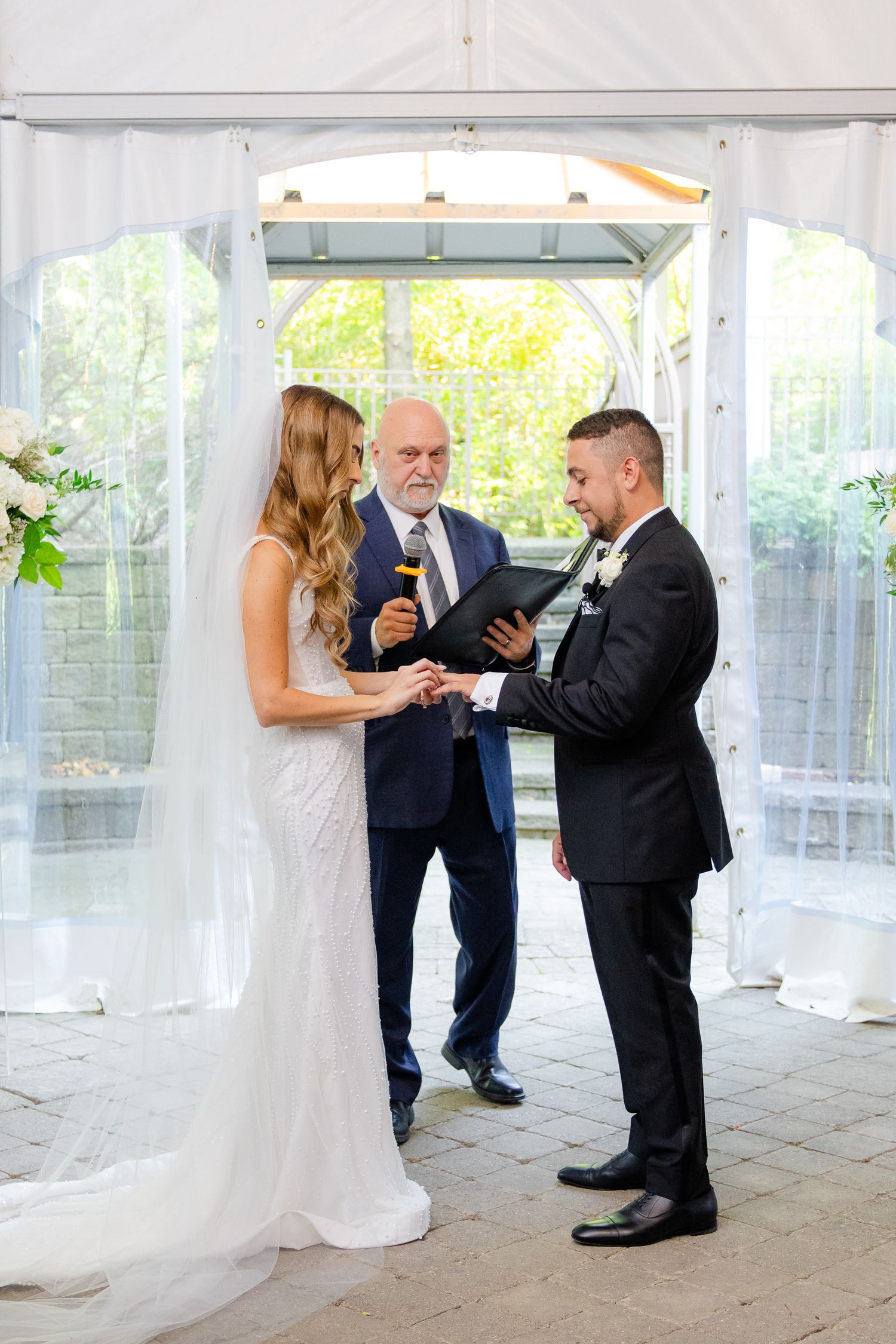 Wedding ceremony showing couple and officiant reviewing ceremony documents under white tent.