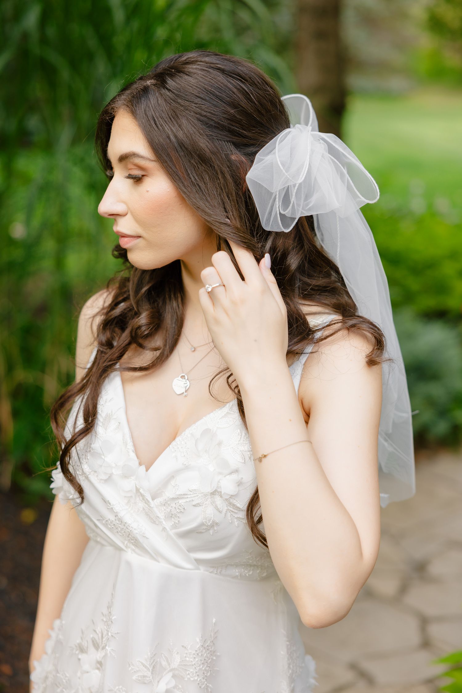 Side profile of bride in white dress with veil showing delicate jewelry details.