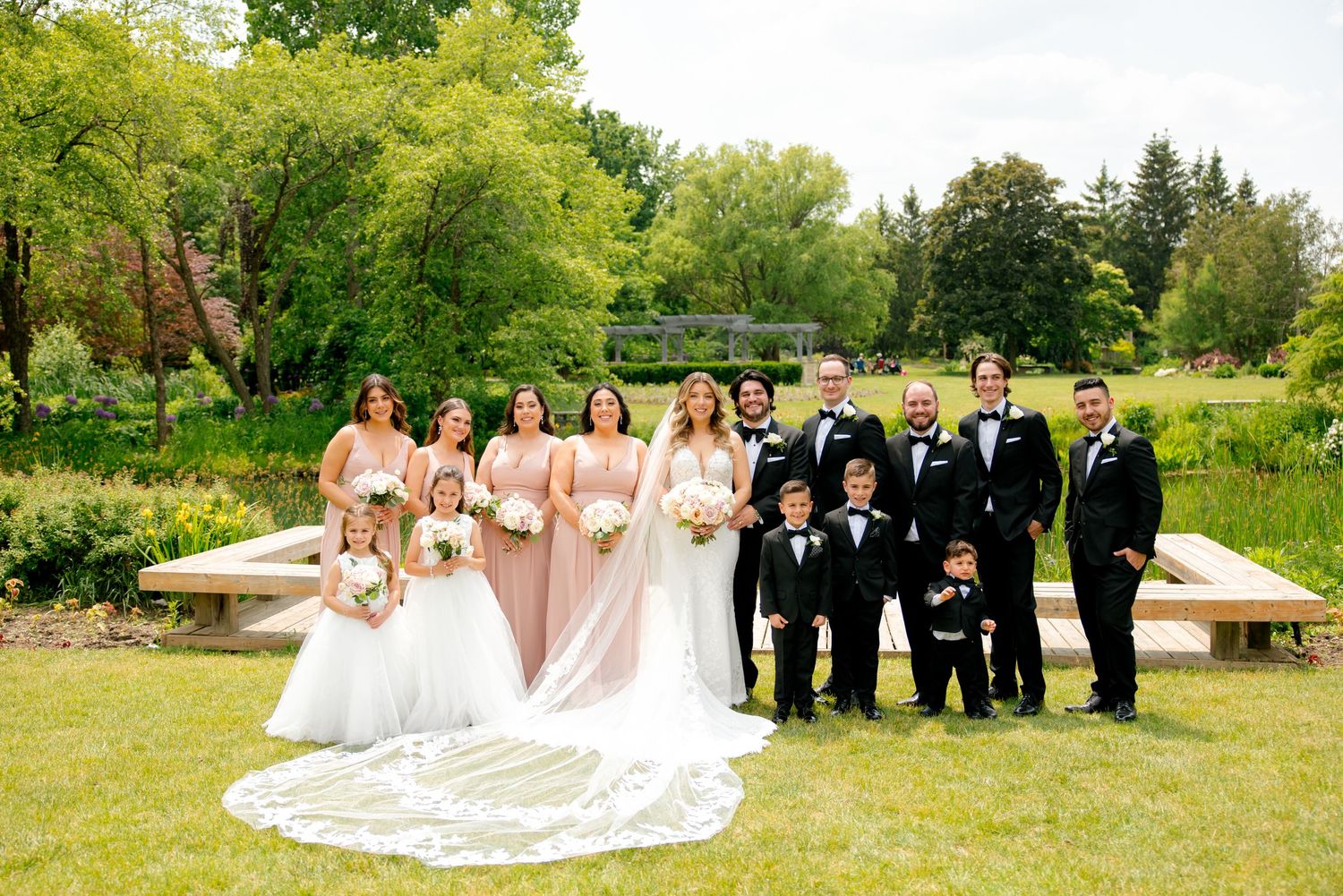 Bridal party in coordinated pink and black attire gathered for outdoor garden photo.