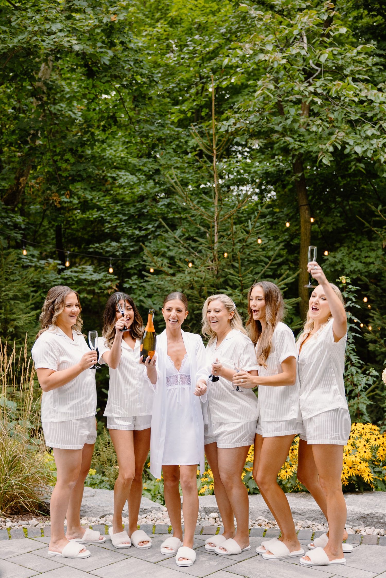 Celebration scene with group in white outfits toasting with champagne in a garden setting.