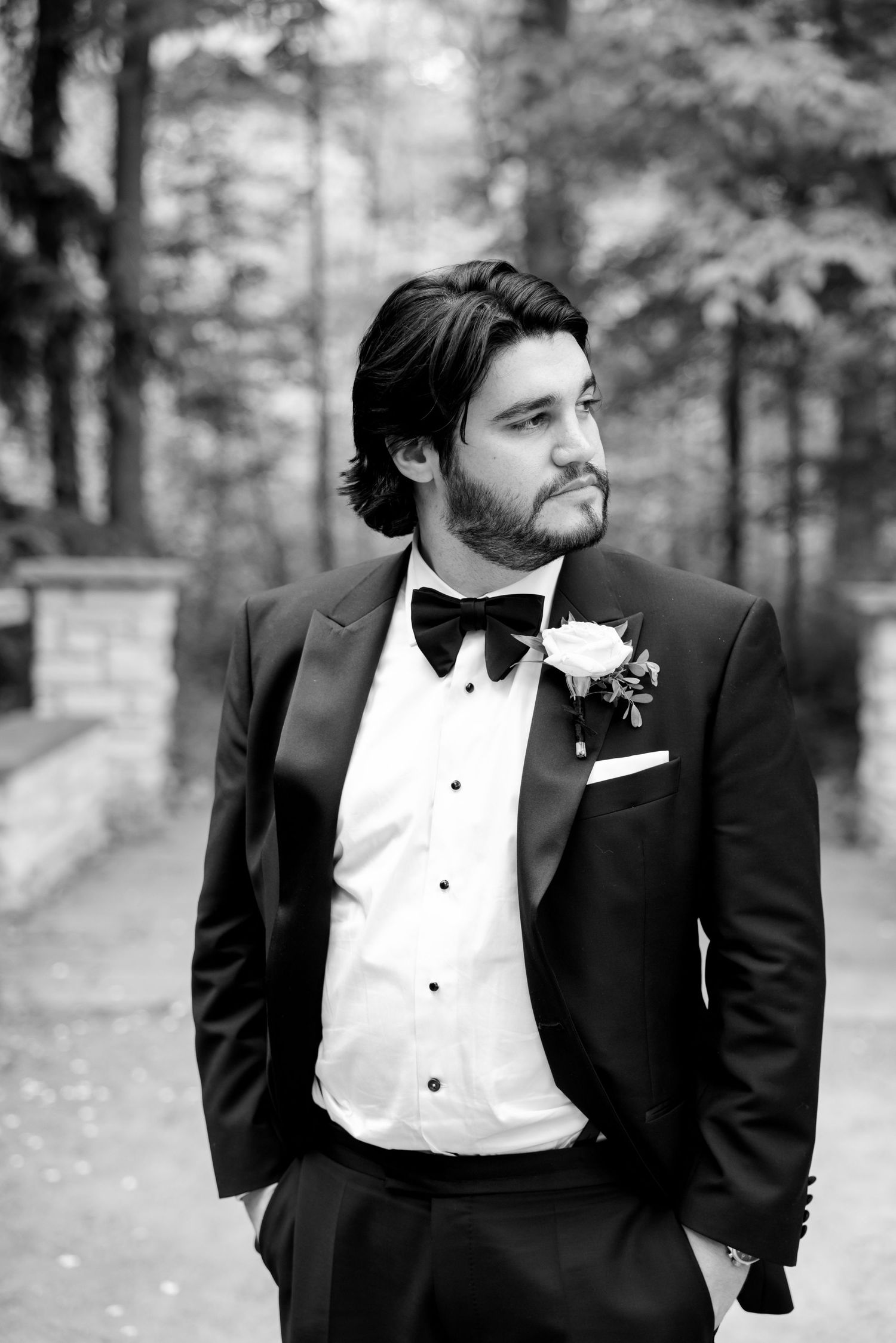 Black and white portrait of a groom in formal attire standing outdoors with a thoughtful expression.