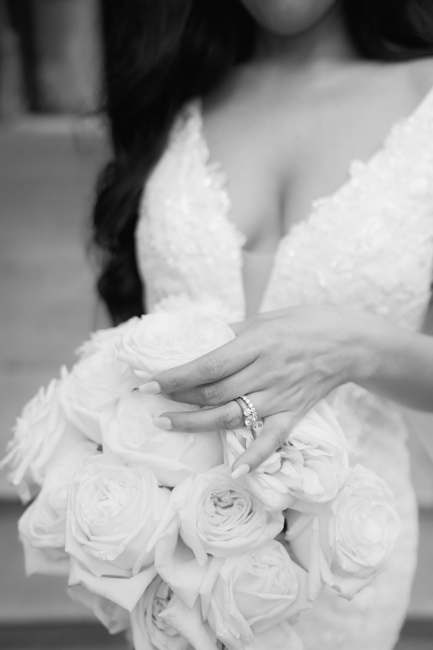 Close-up detail of white rose bouquet and wedding rings with lace dress in black and white.