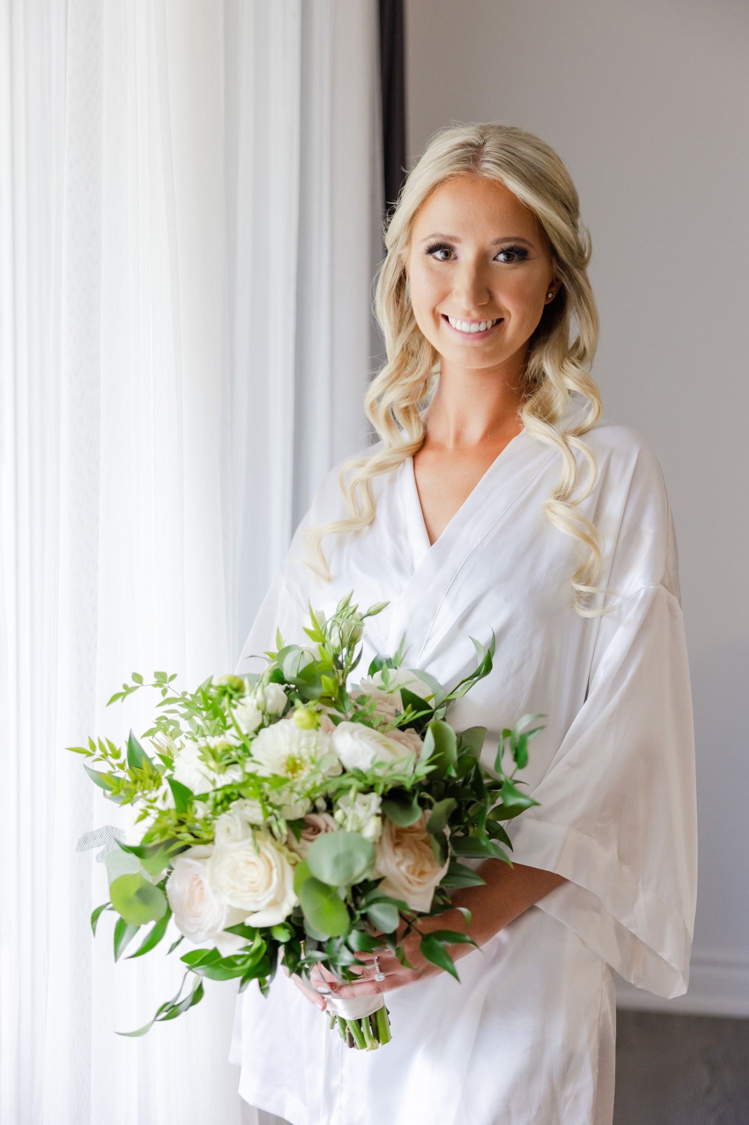A wedding day preparation scene with someone holding a lush white and green bouquet.