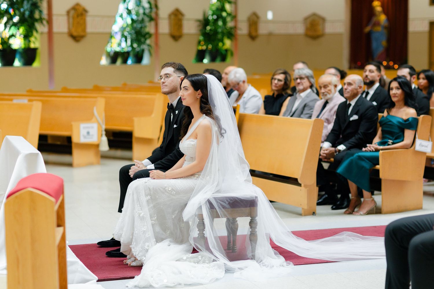 A wedding ceremony in progress with guests seated in wooden pews while the couple sits at the altar.