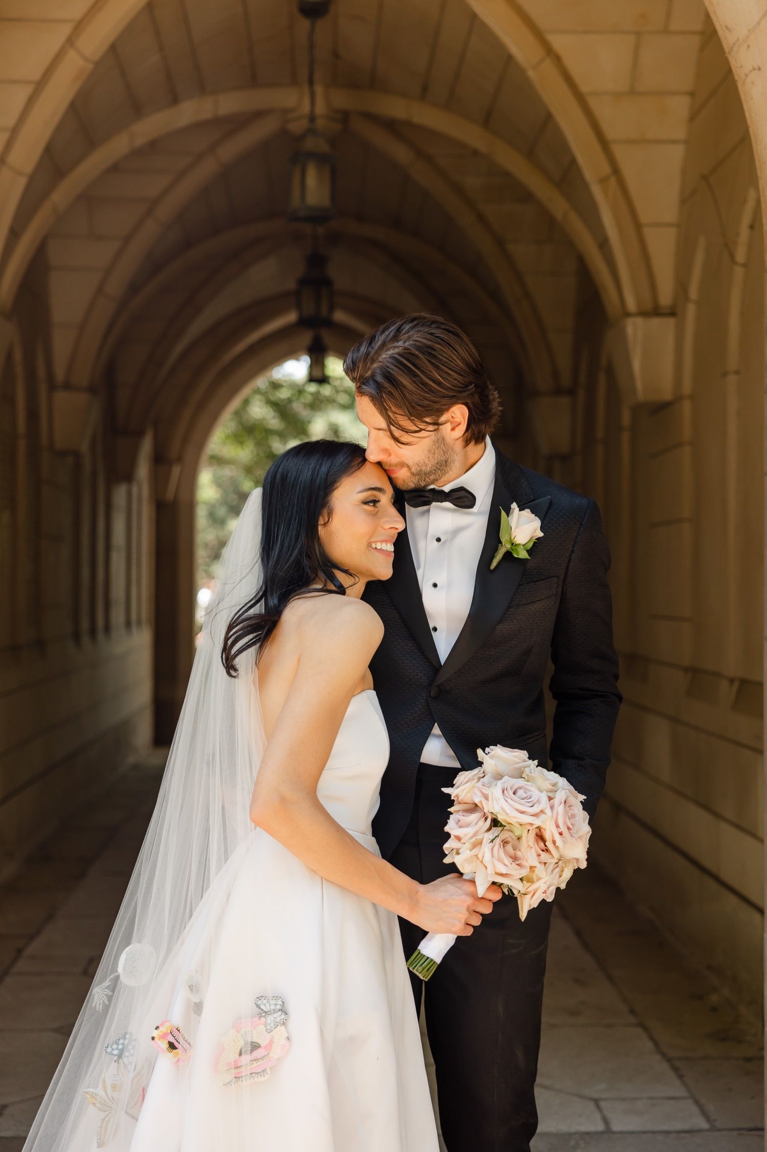 Tender wedding portrait in stone corridor with soft natural lighting.