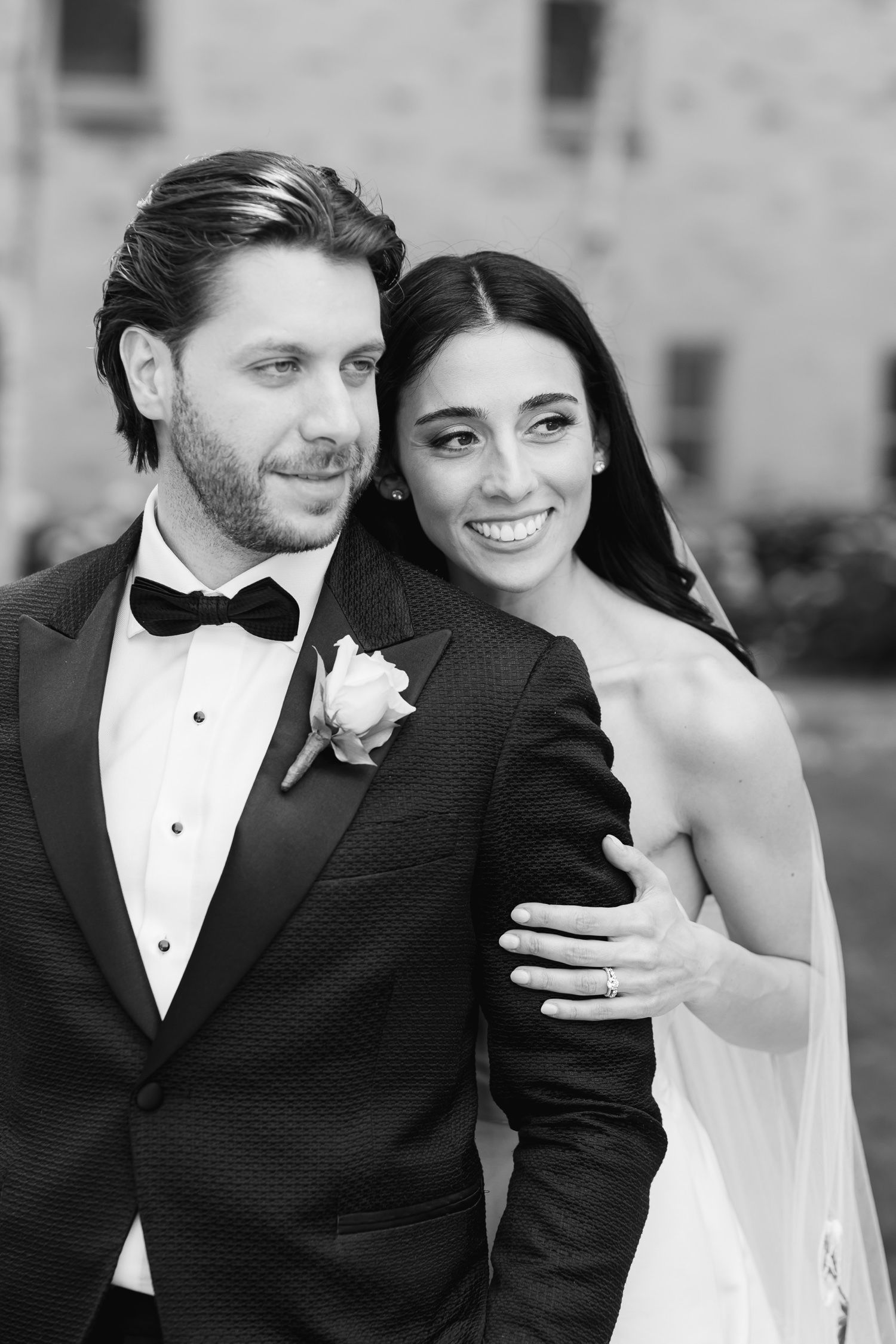 Black and white portrait of newlyweds sharing an intimate moment against a stone wall backdrop.