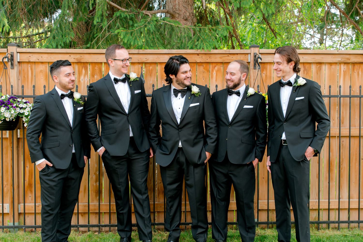 Group of five men in formal black tuxedos stand together at outdoor event.