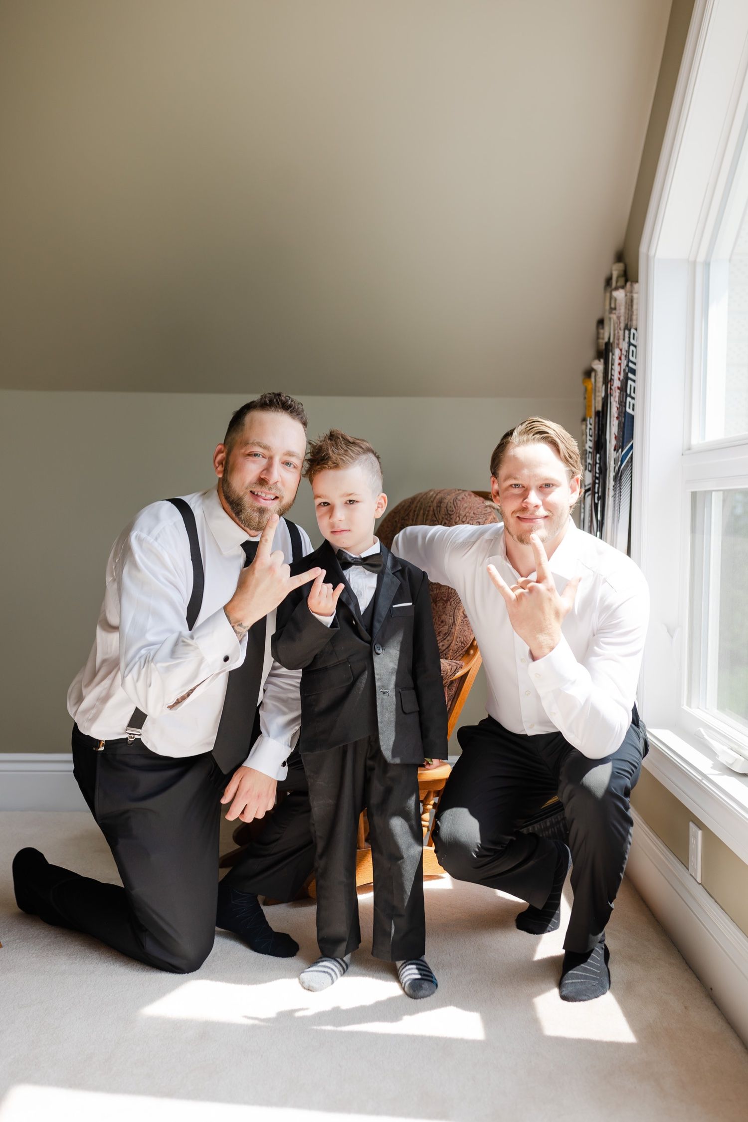 A formal group portrait showing people in suits and bow ties posing together by a window.