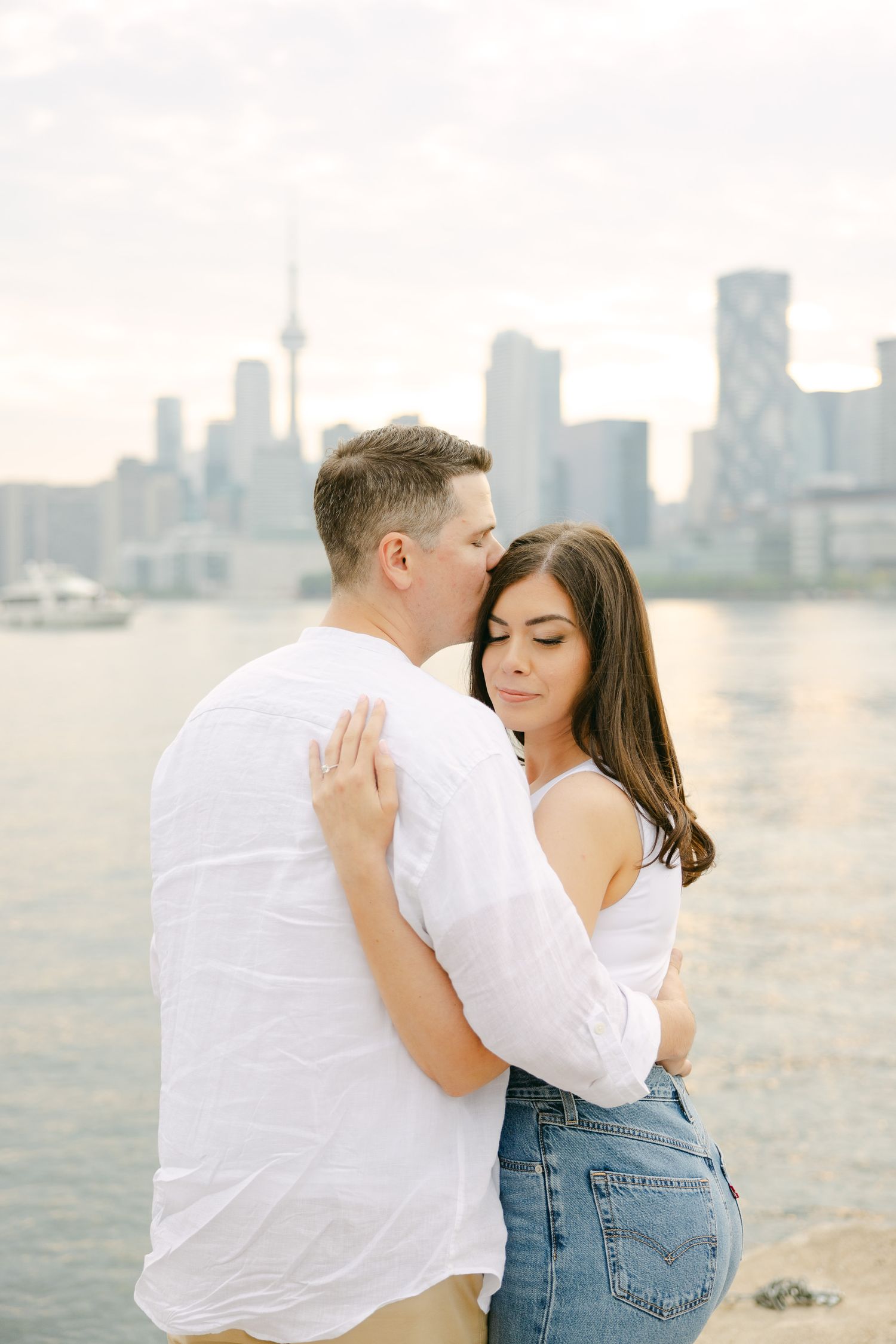 A couple shares a romantic moment by the lake with Toronto's downtown towers in the distance.