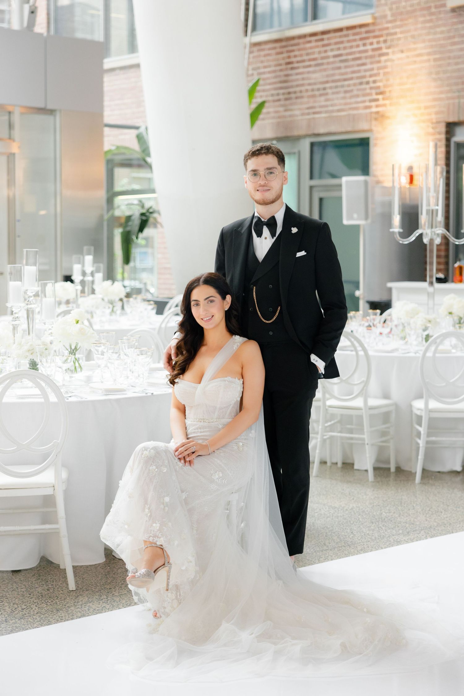 Couple posing in formal attire amid elegant white wedding reception decor.