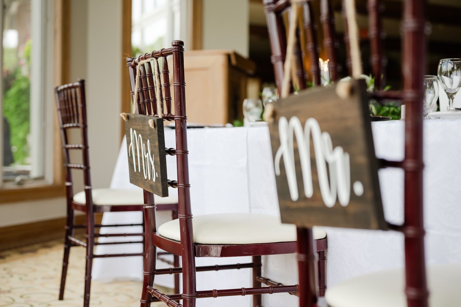Dark wooden chiavari chairs with white seat cushions arranged at a wedding reception.