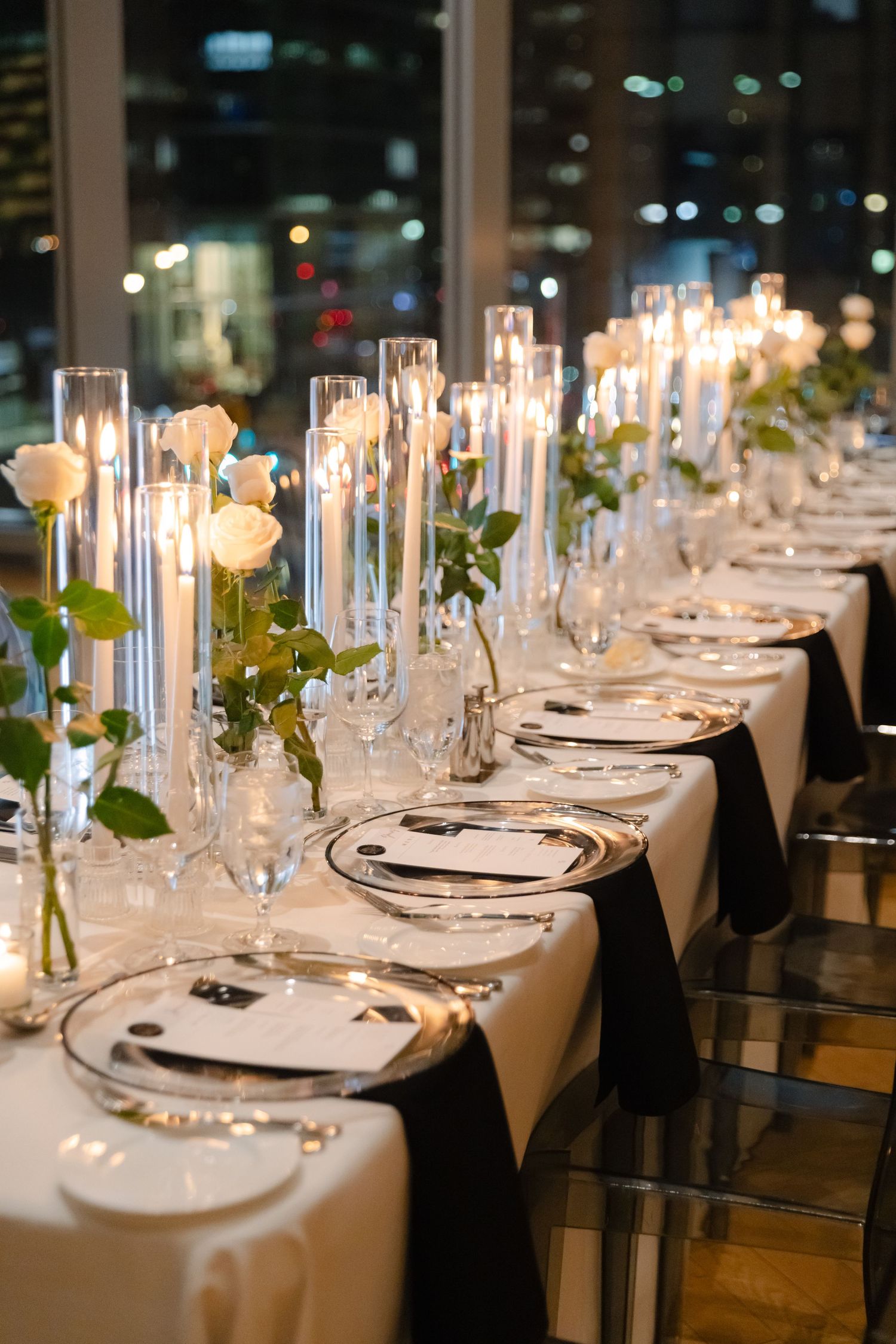 Long banquet table with crystal candlesticks and elegant place settings against city lights.