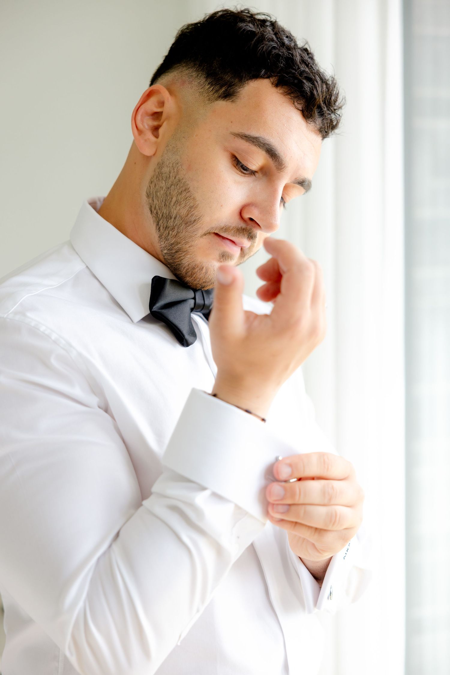 Person in formal white shirt and bow tie adjusts collar in contemplative pose.