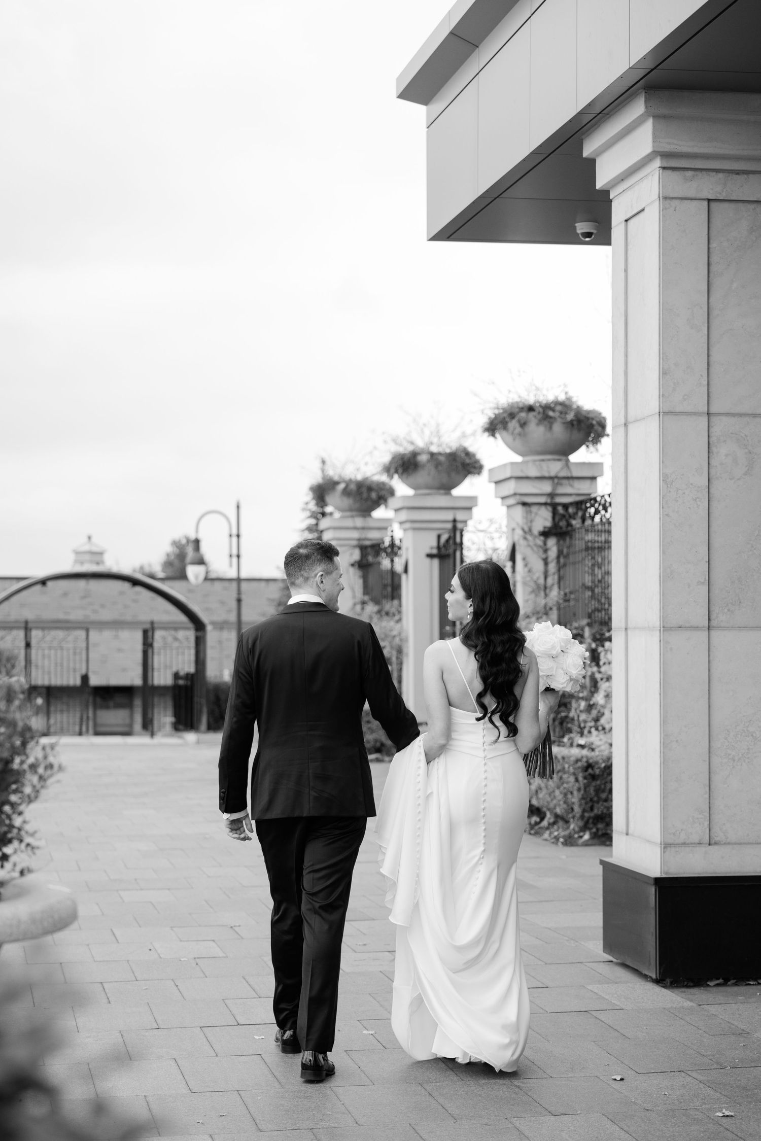 Black and white photo of a wedding couple walking along a columned promenade.
