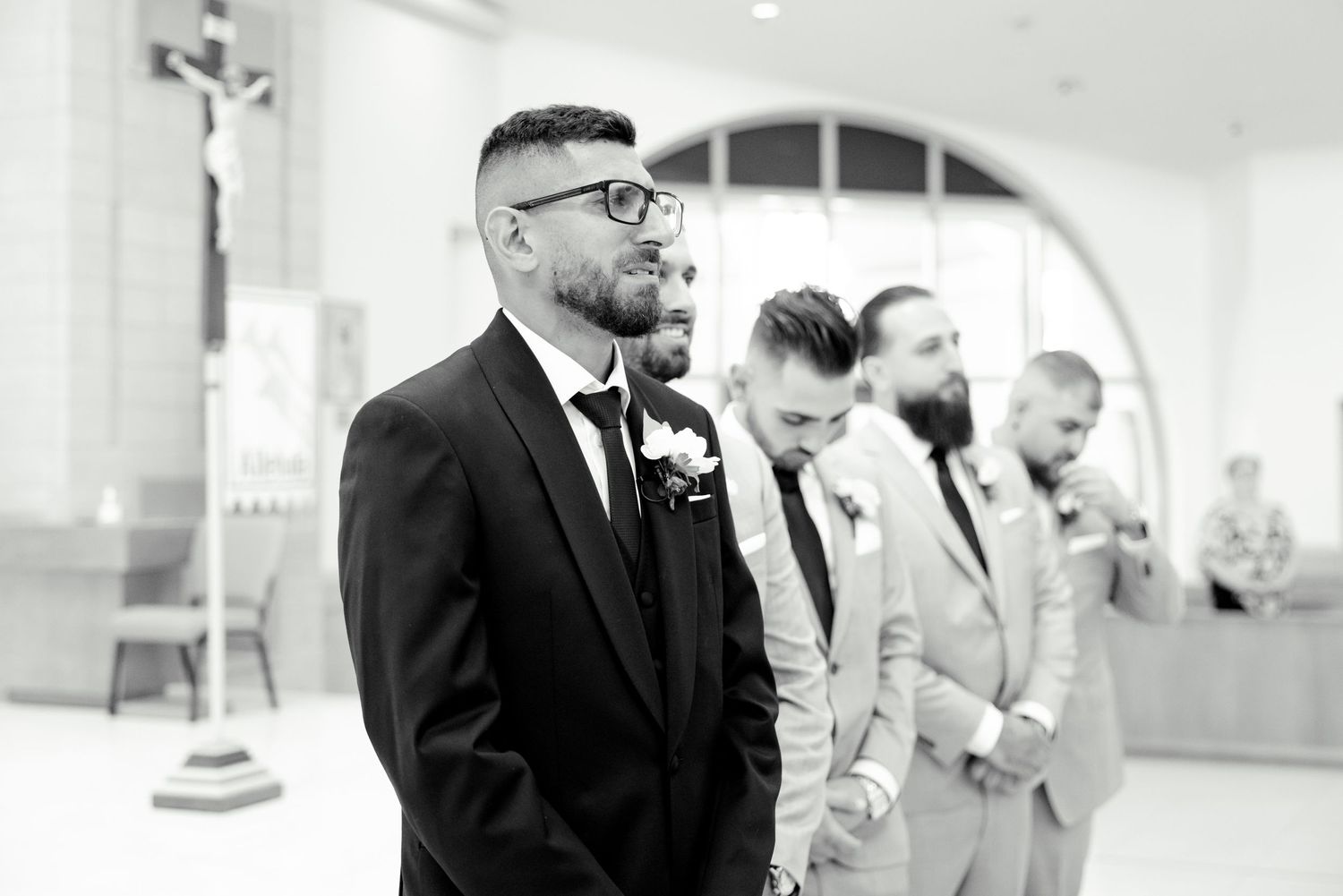 A black and white candid photo of groomsmen standing in a church.