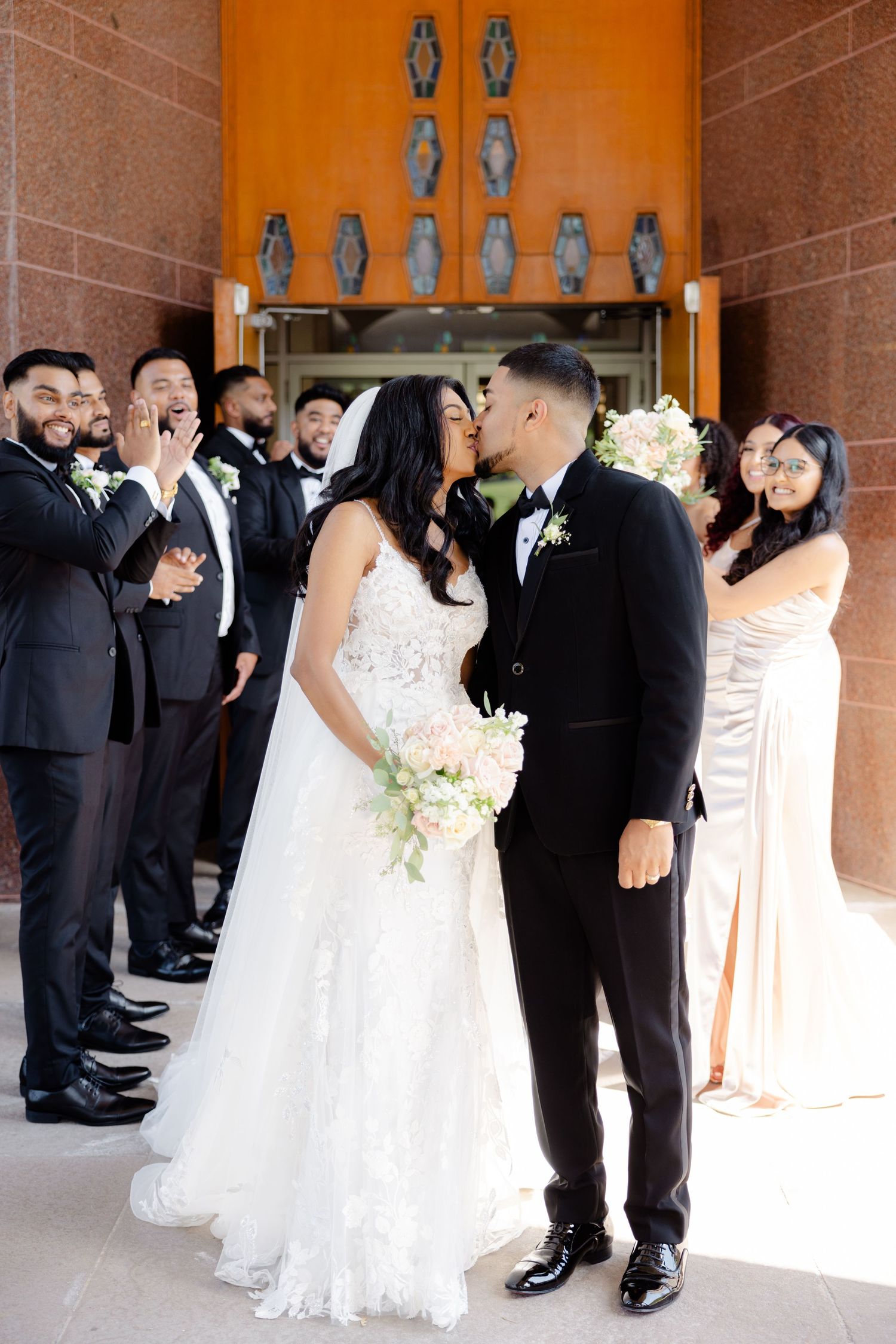 Joyful wedding party celebrates during formal exit photos at ornate church entrance.