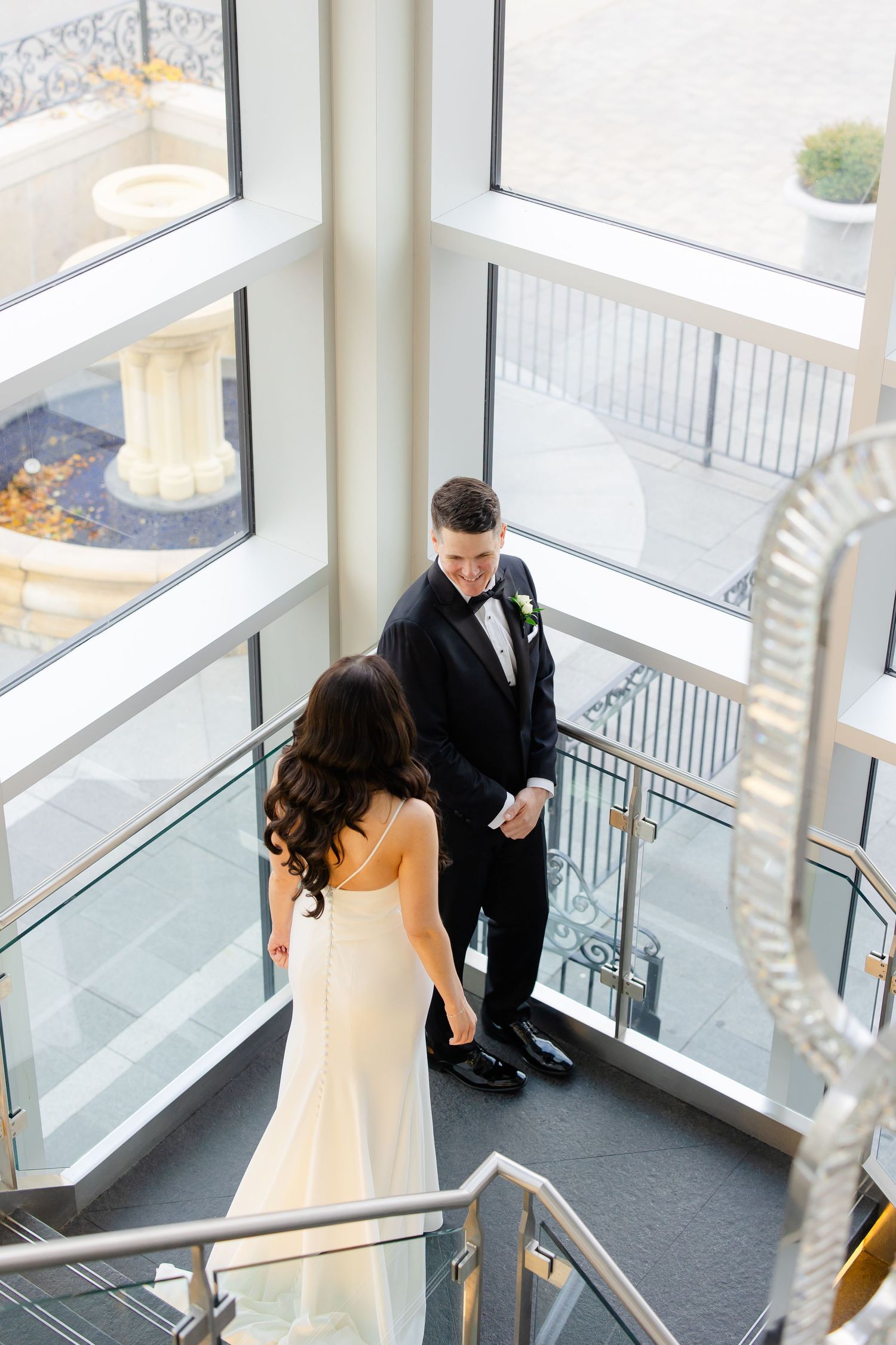 A bride and groom share their first look moment in a modern venue with large windows.