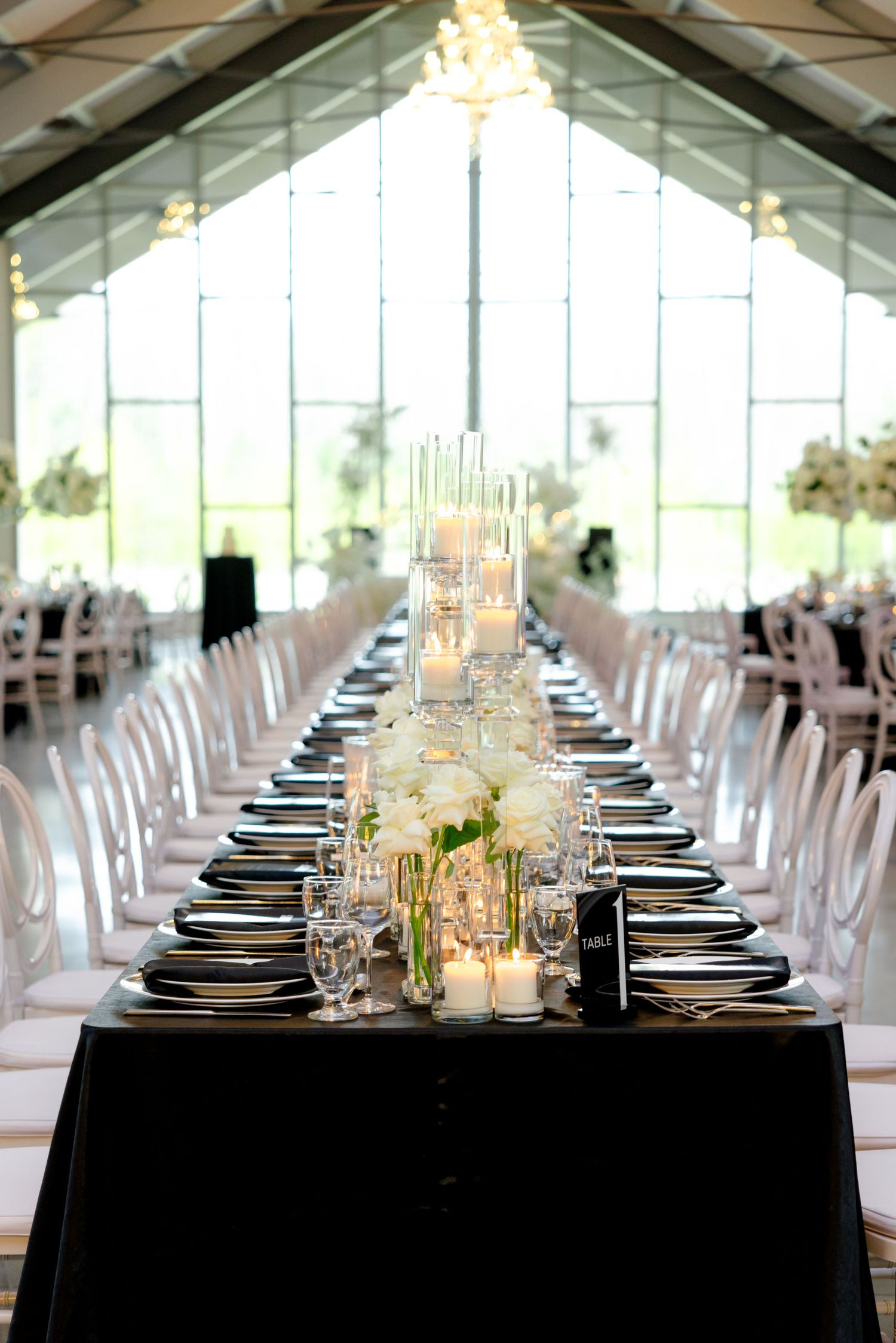 An elegant wedding table setting with black linens, candles and white floral arrangements.
