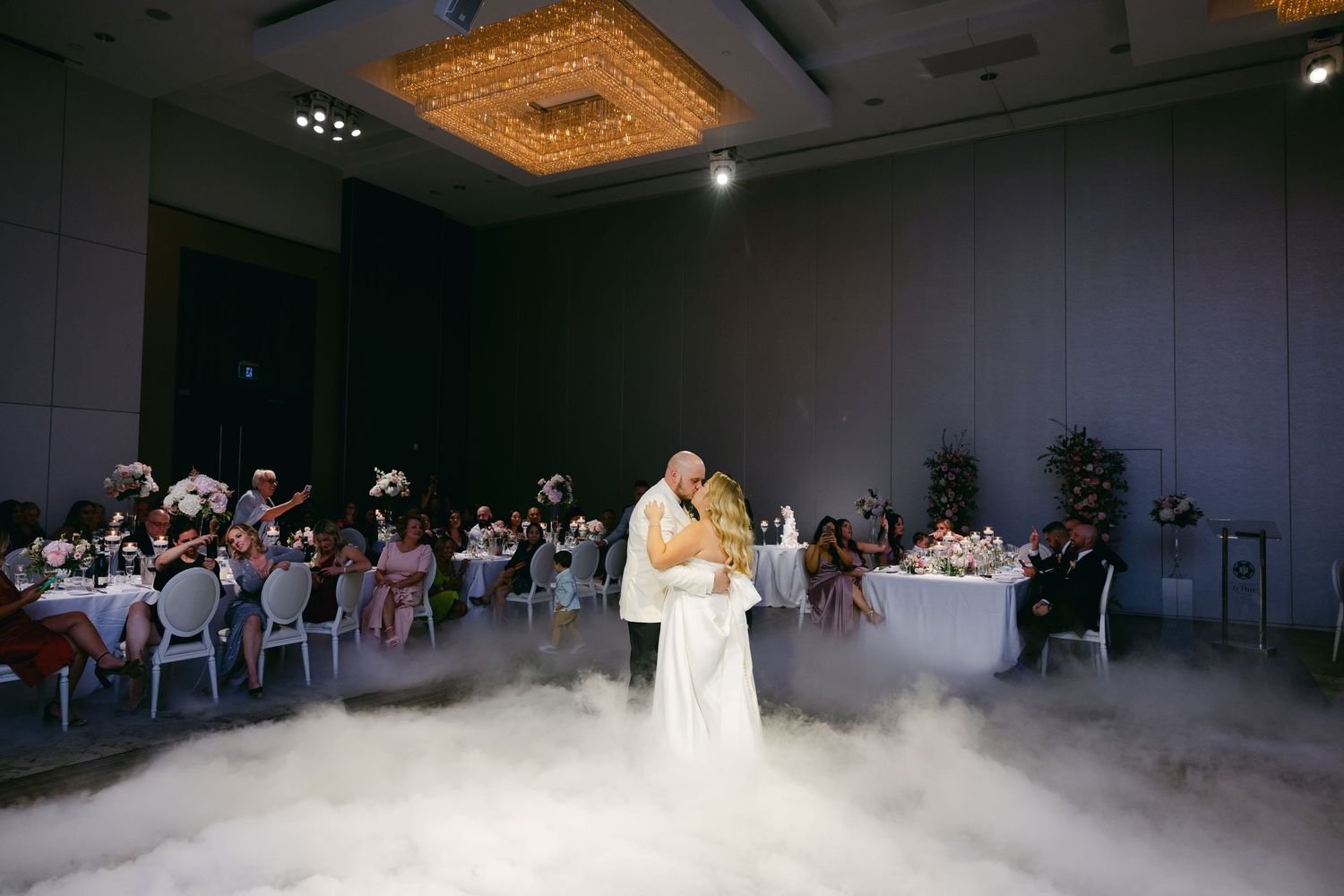 Wedding couple dances in cloud-like fog while reception guests watch from their tables.