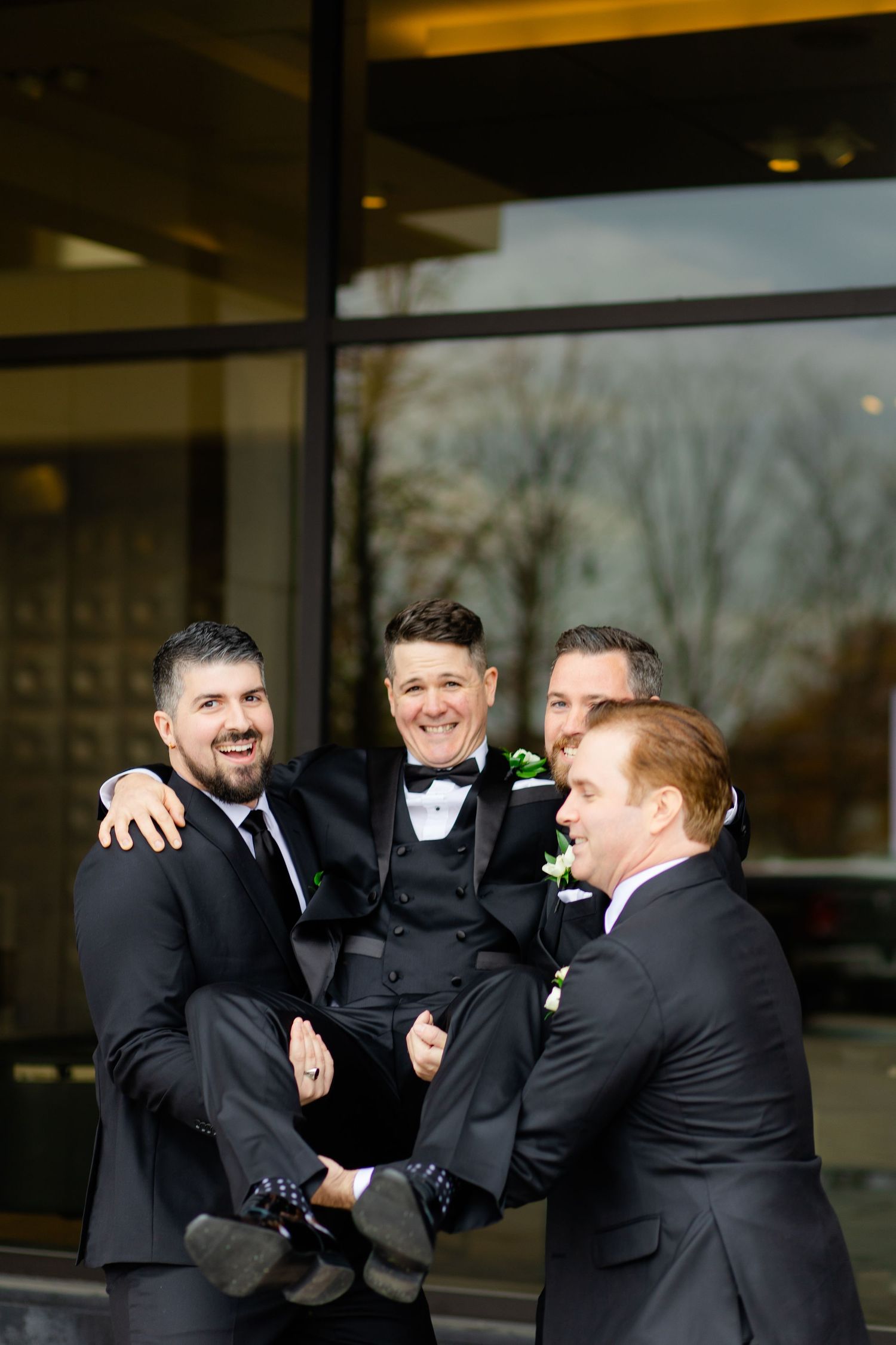 Groomsmen lift and carry groom in playful moment during wedding photo session.