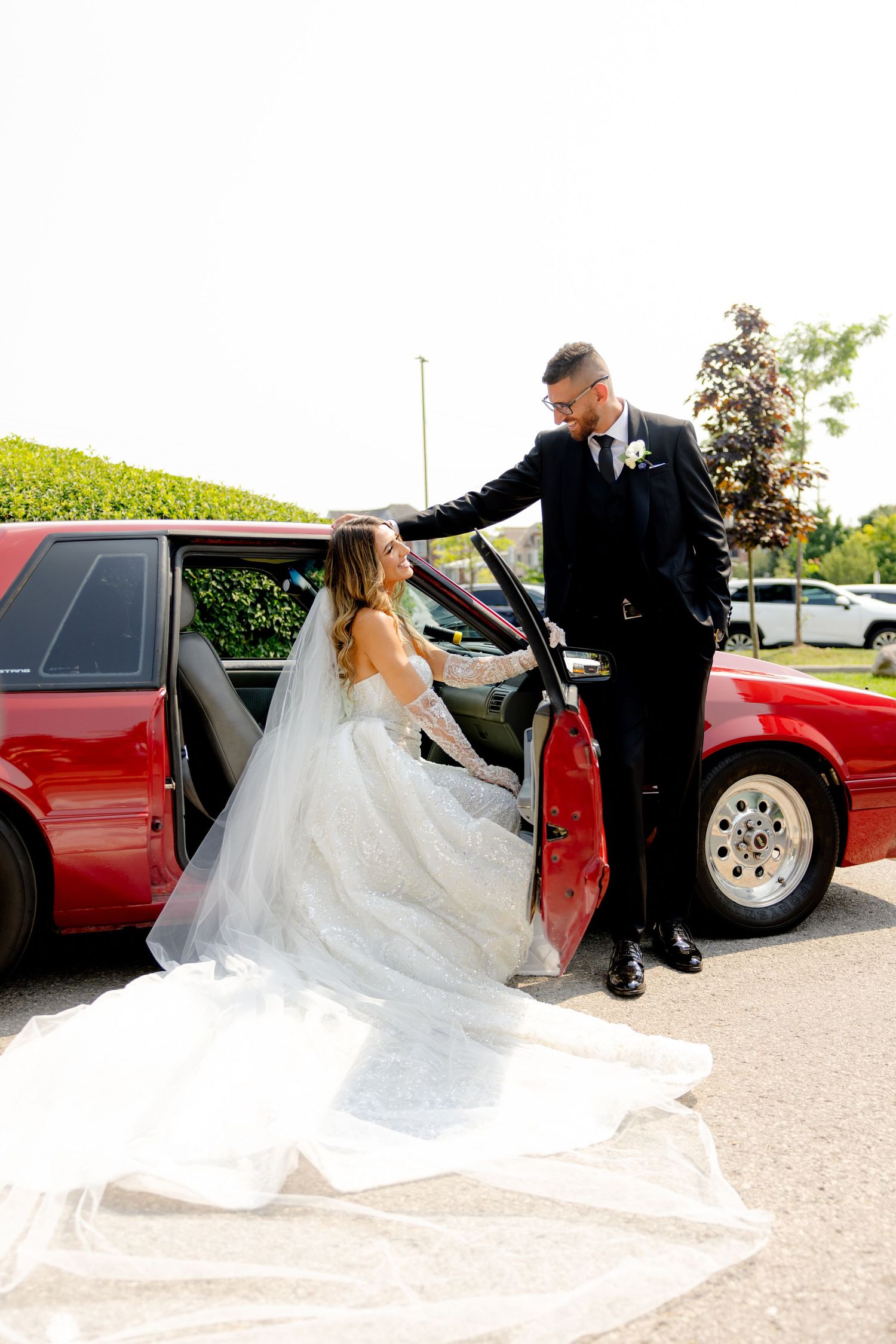 Candid moment of a couple by their red car during their wedding photoshoot.
