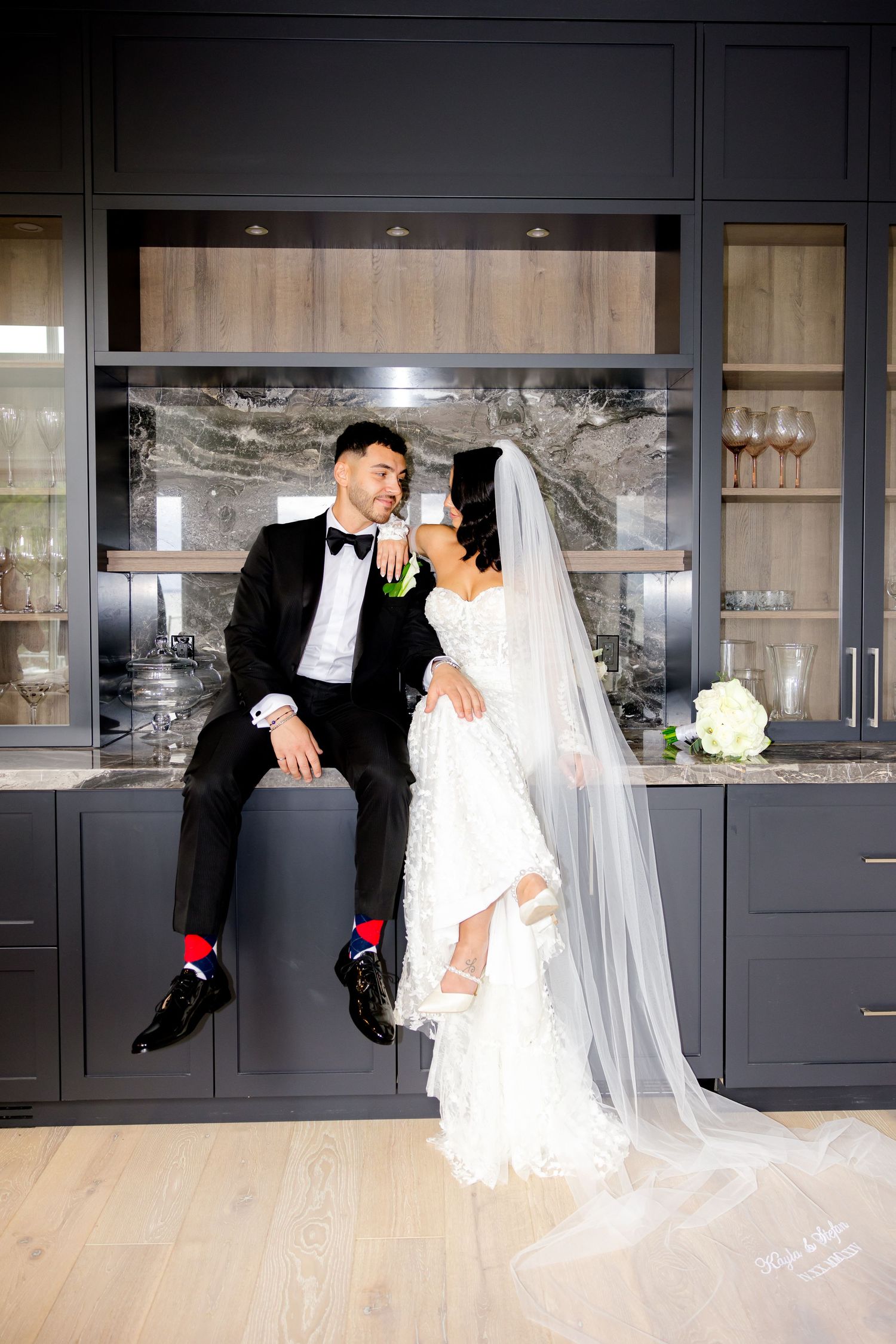 A candid wedding moment captured in front of sleek kitchen cabinetry with a marble backsplash.