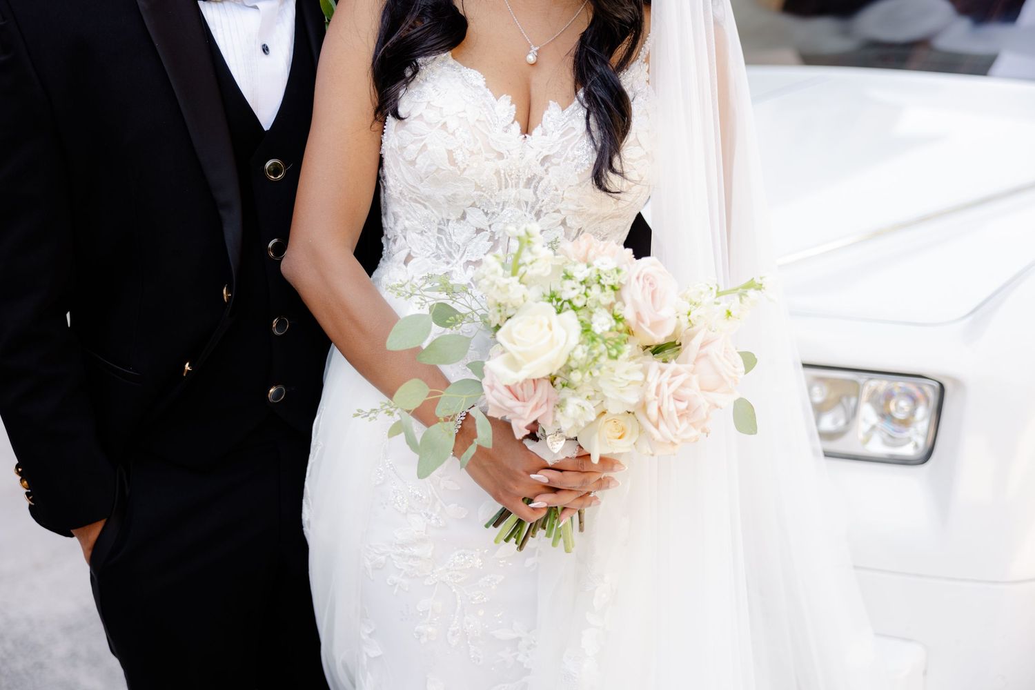 Close up of bride holding delicate bouquet of white and pink flowers with groom beside.