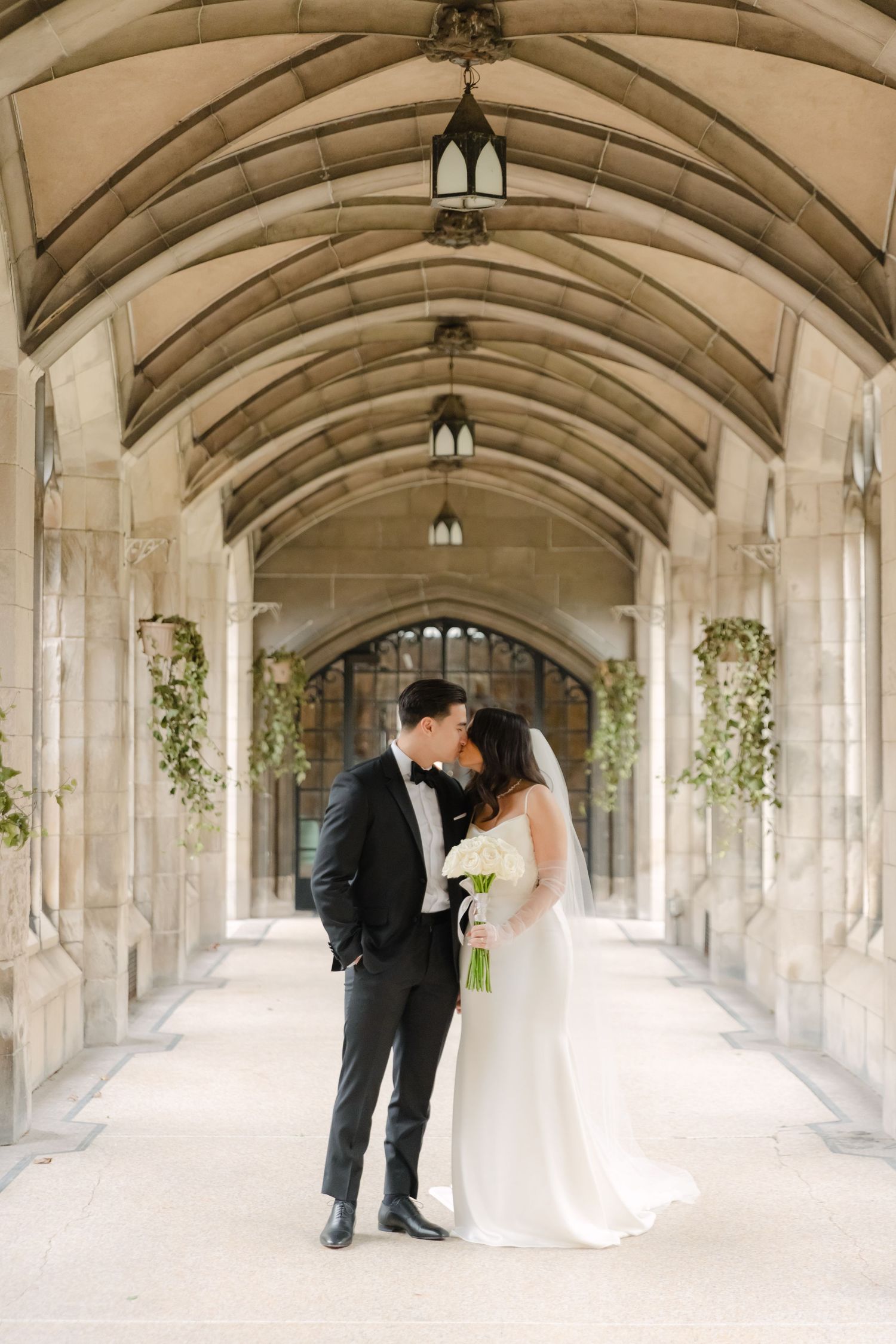 Romantic wedding portrait in Gothic corridor with streaming natural light and floral decor.