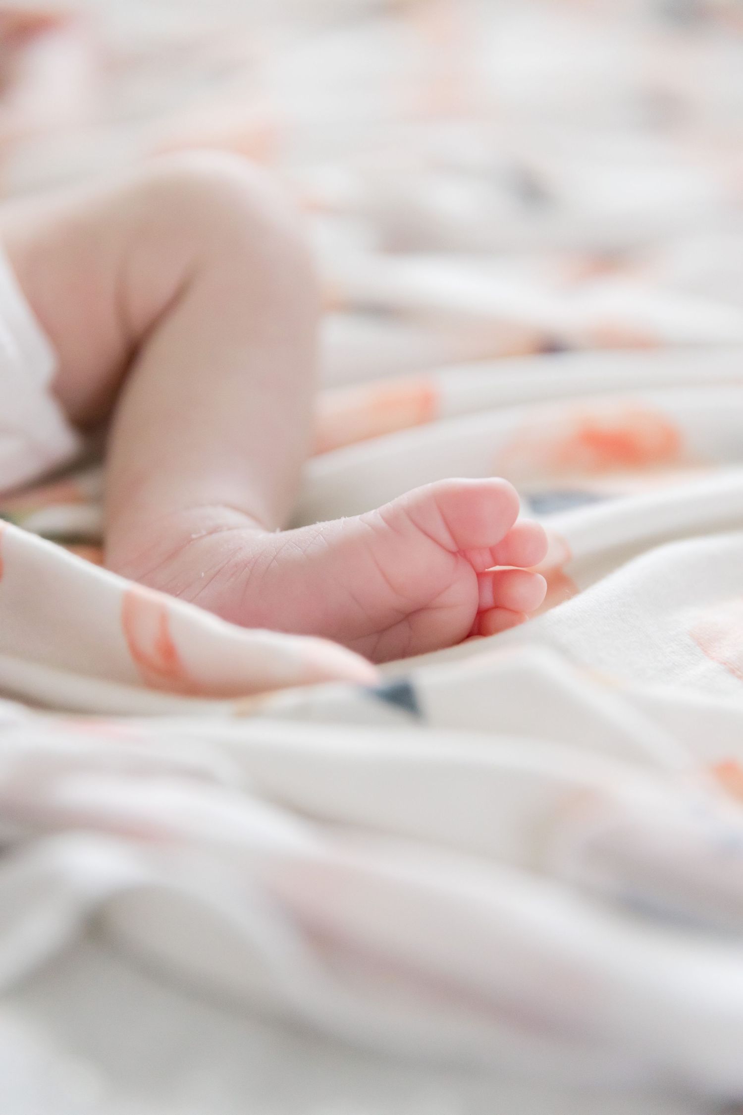 Close-up of tiny newborn baby foot resting on floral patterned blanket.