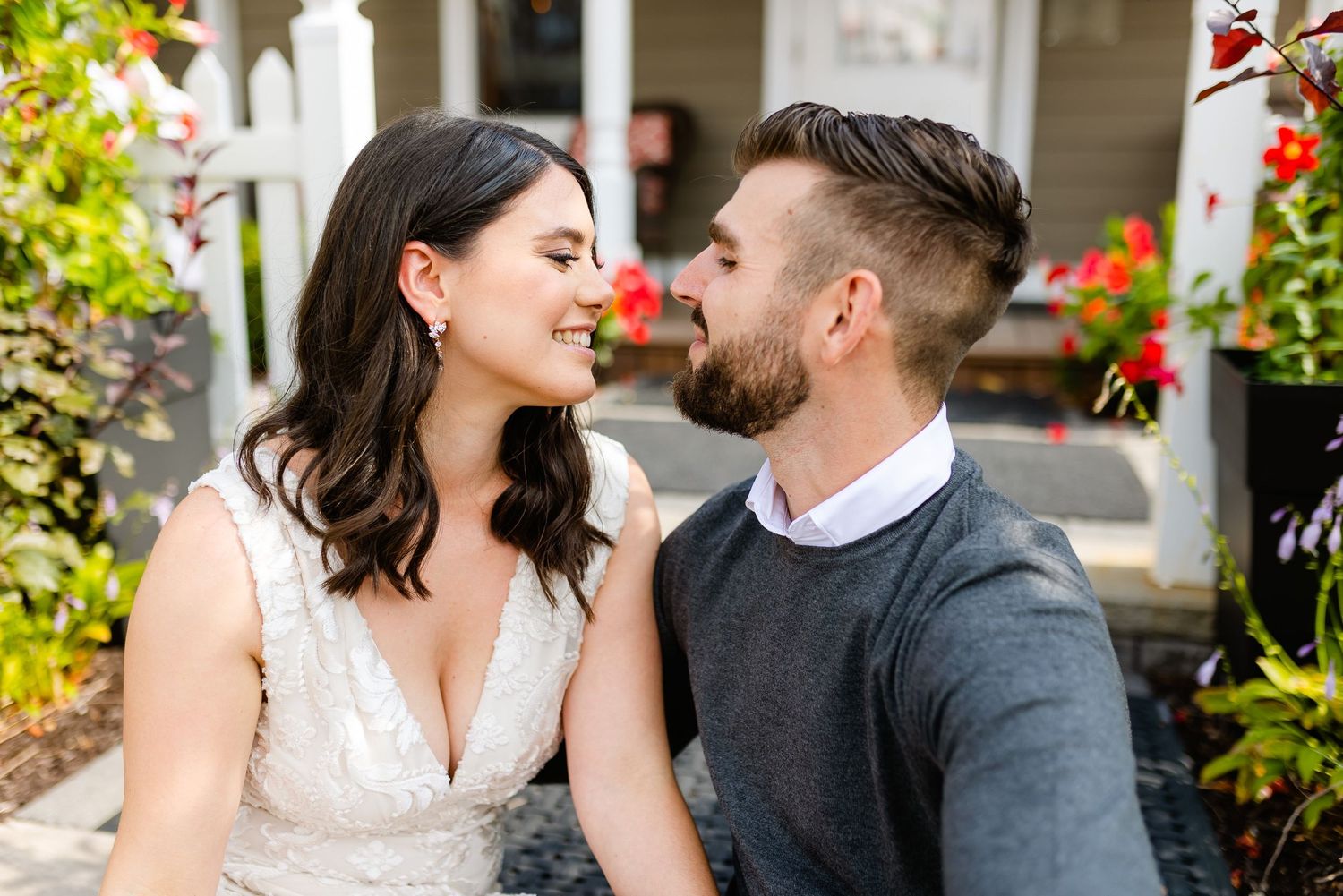 A romantic couple gazes at each other on an outdoor porch with red flowers.