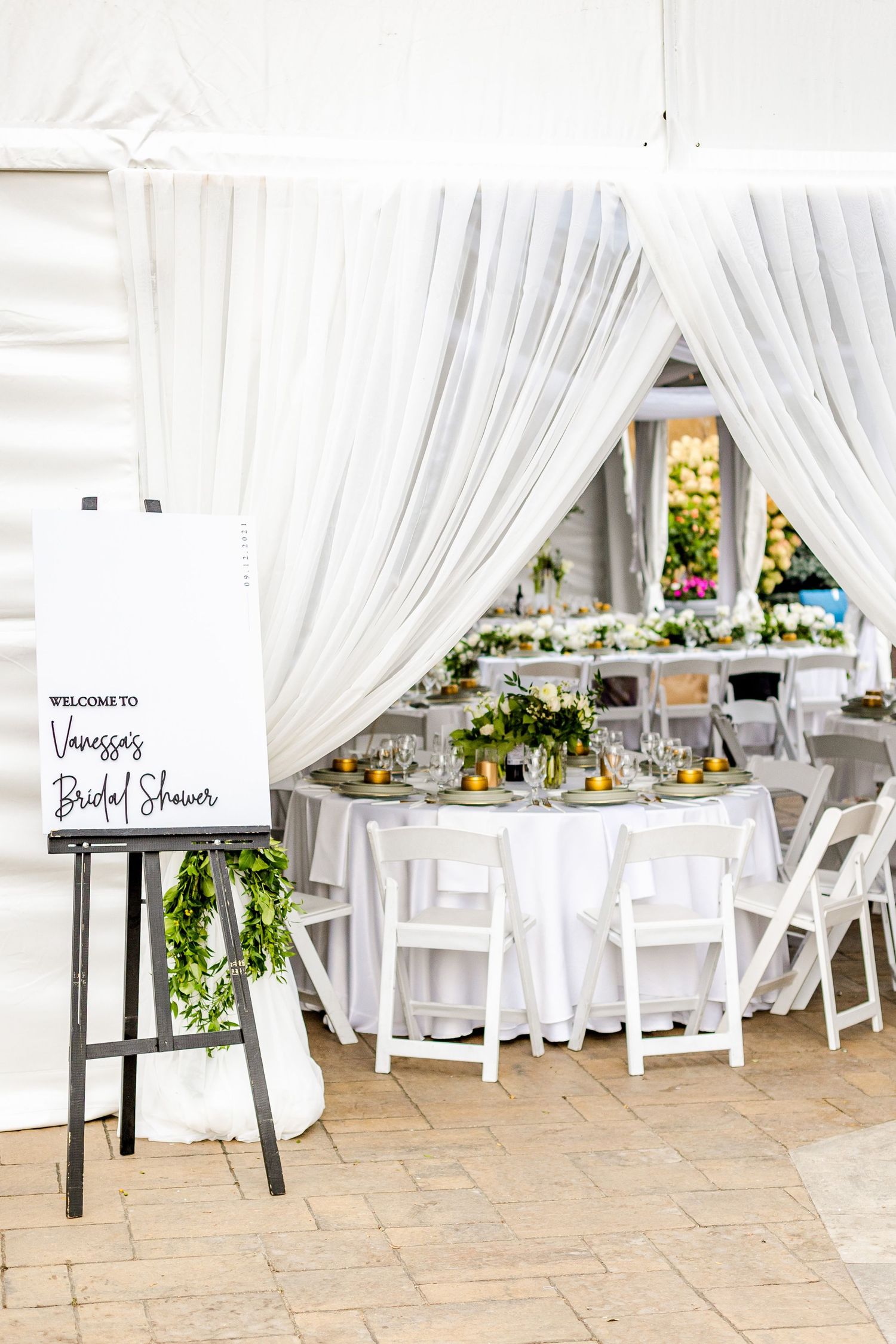 Elegant white draped reception space with round tables and floral centerpieces.
