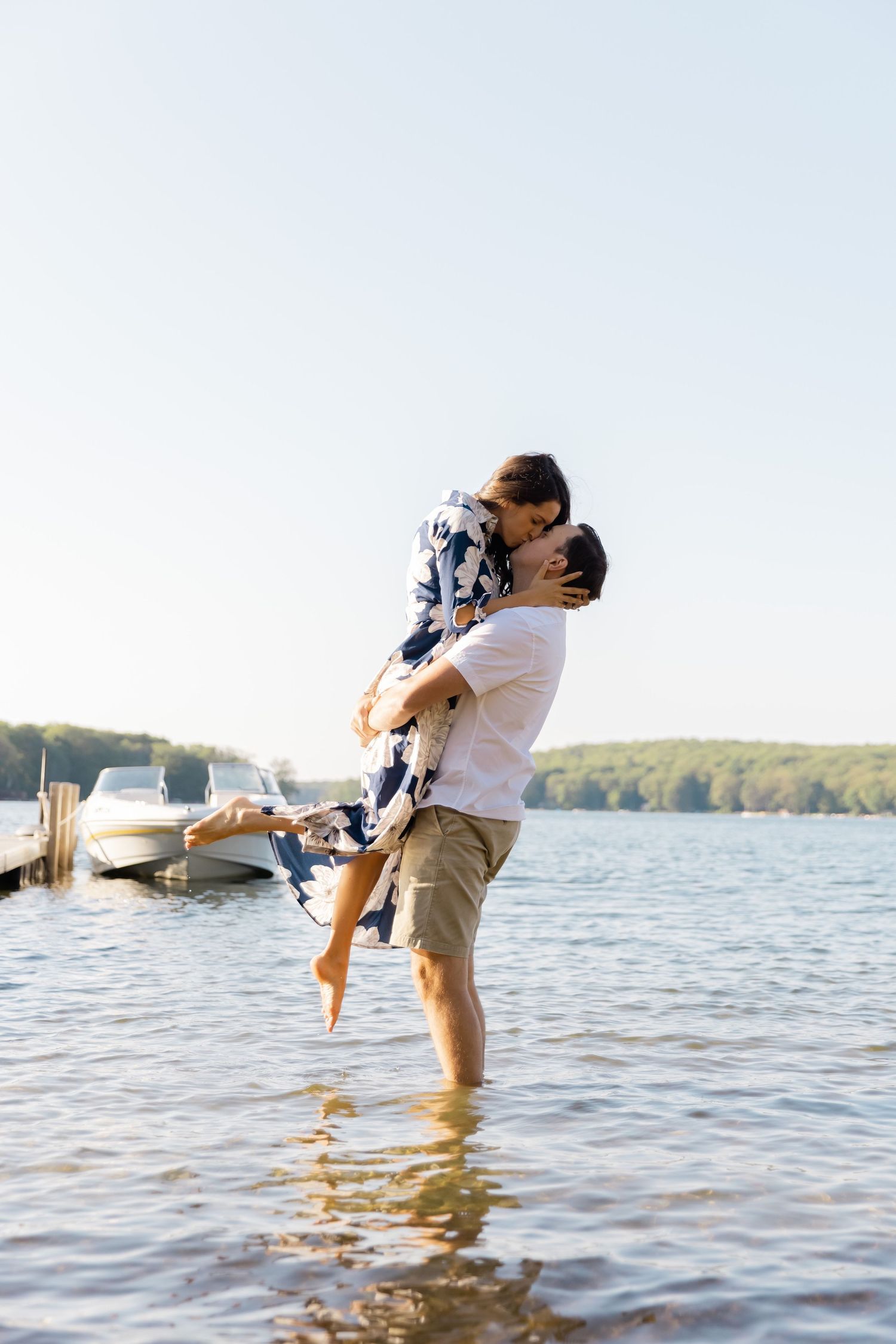 A joyful couple embraces and lifts off the ground in shallow lake water on a sunny day.