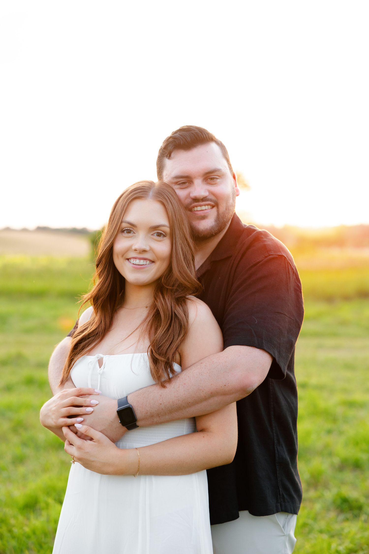 Happy couple embracing in golden sunset light with bright smiles.