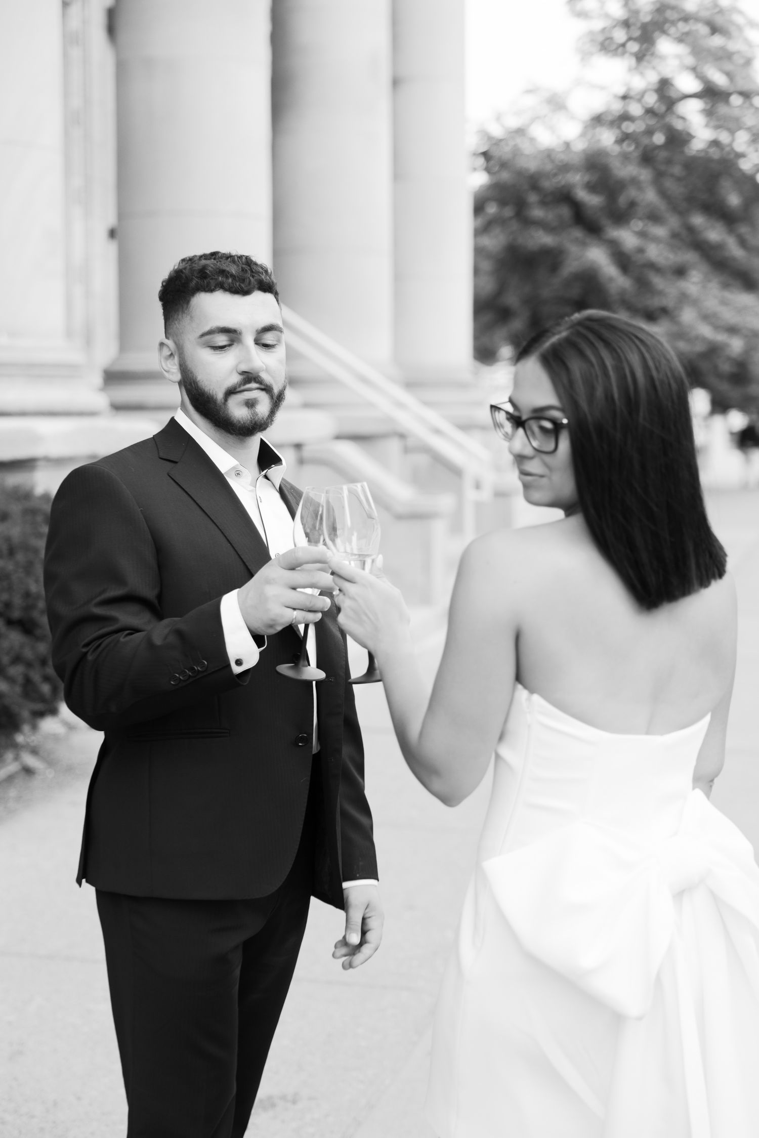 Black and white photo of couple toasting with wine glasses in front of historic building.
