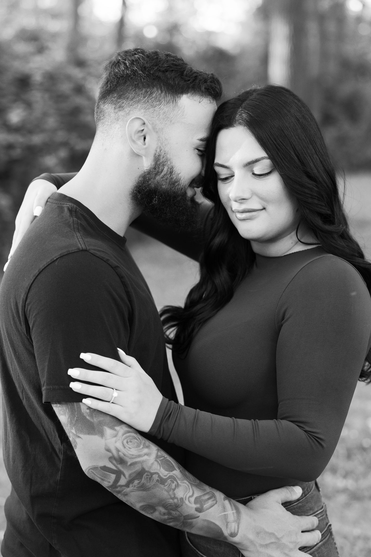 A black and white portrait captures a tender moment between a couple in nature.