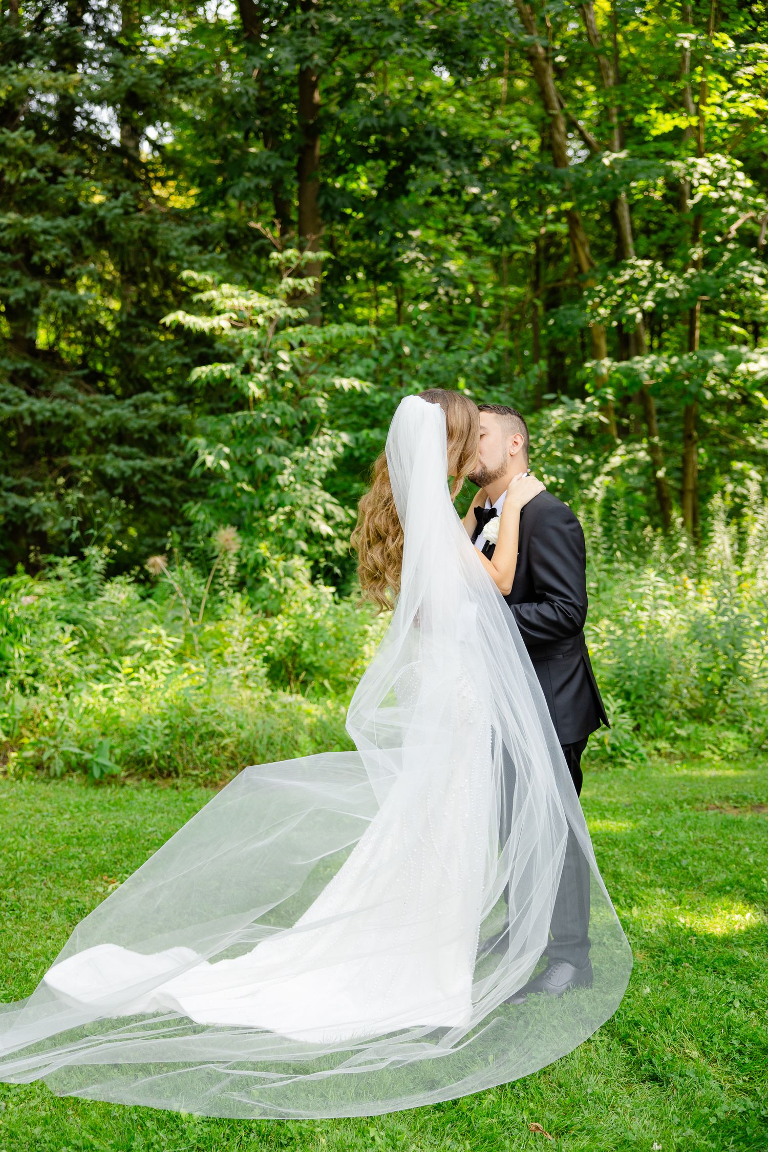 A dramatic wedding photo with a flowing cathedral veil in a scenic garden setting.
